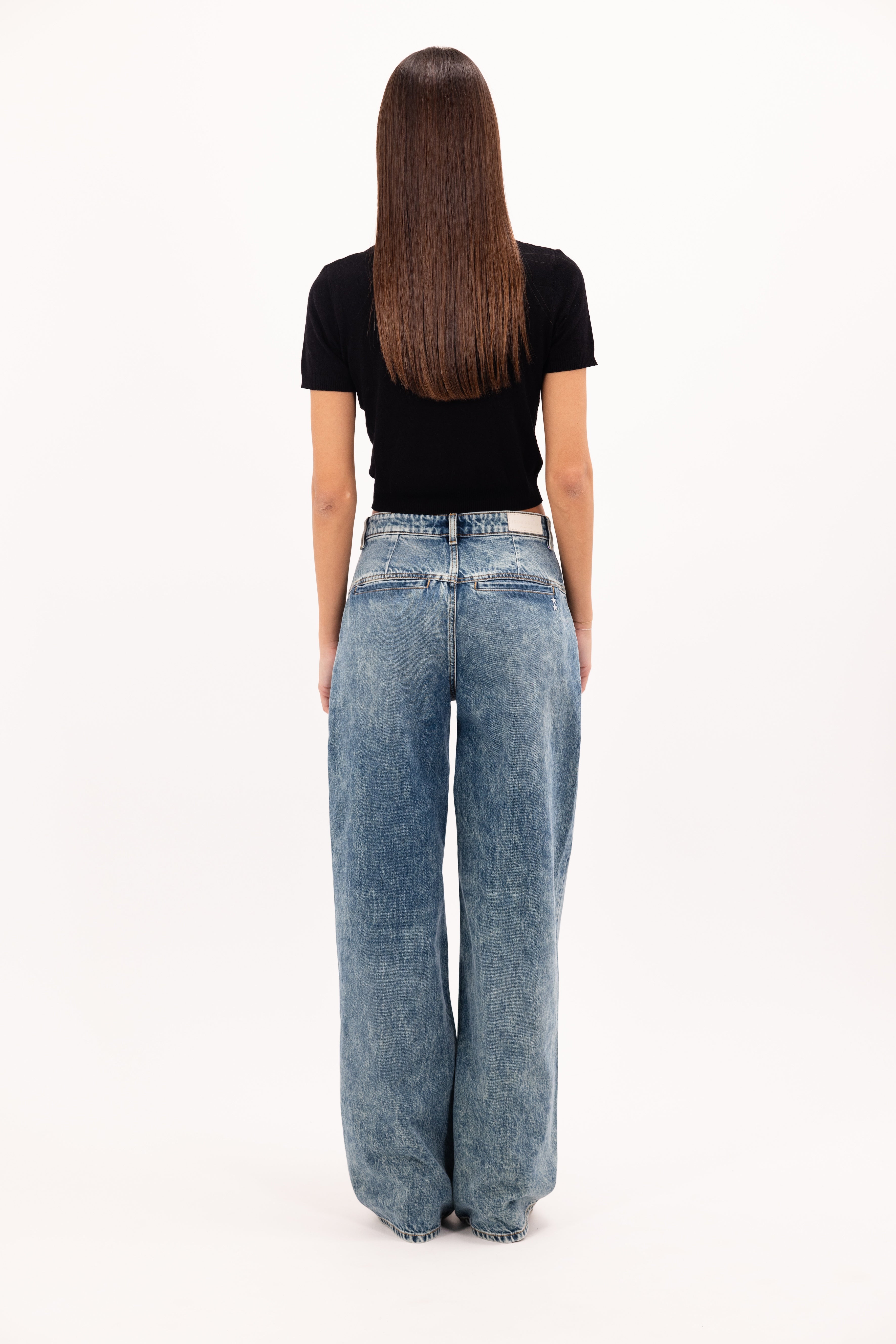 Back view of Ava women’s wide leg jeans in aged stone wash, 100% rigid cotton denim, worn by a model with a black top.