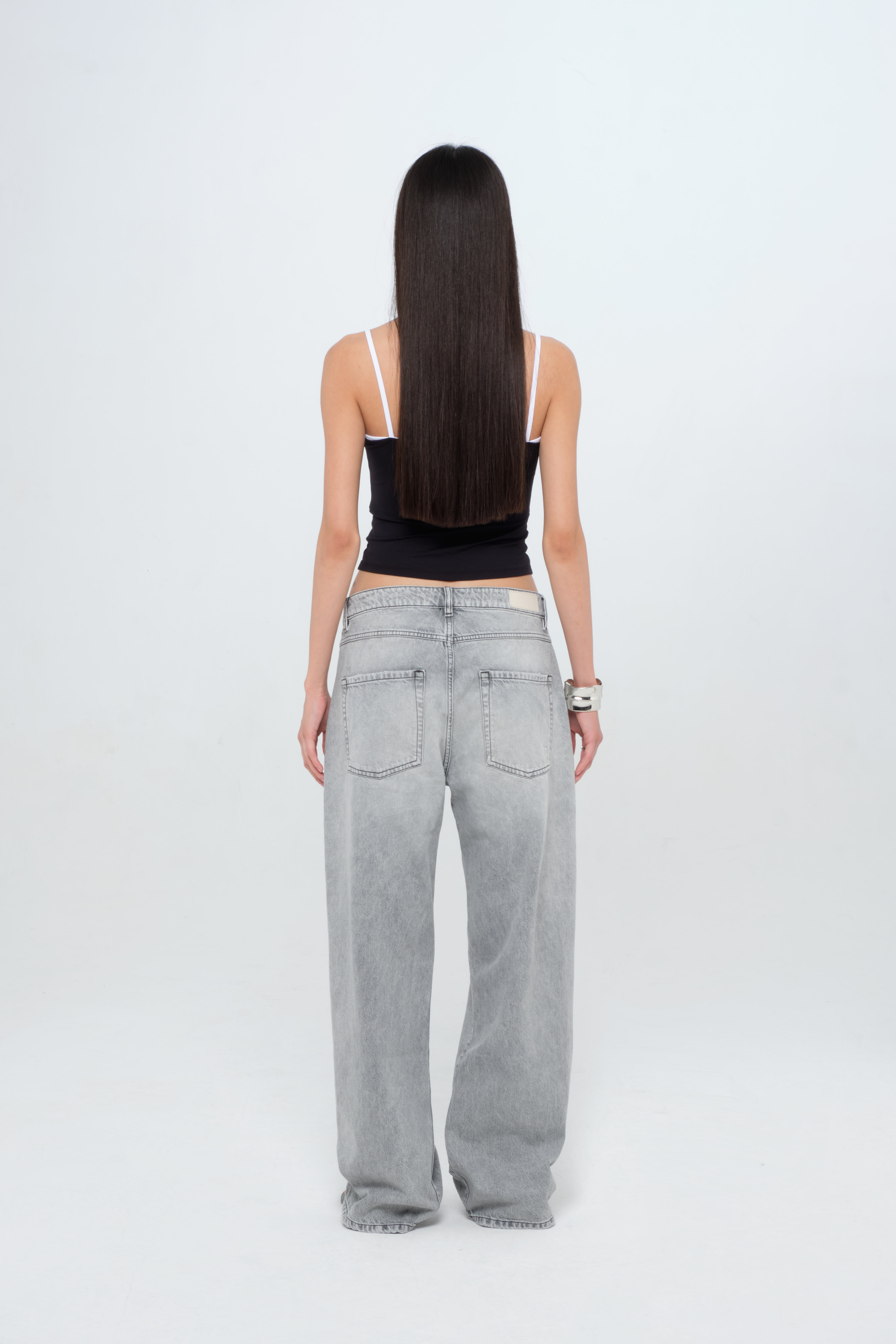 Back view of Bea women’s wide leg jeans in gray wash, 100% rigid cotton denim, worn by a model with a black top.