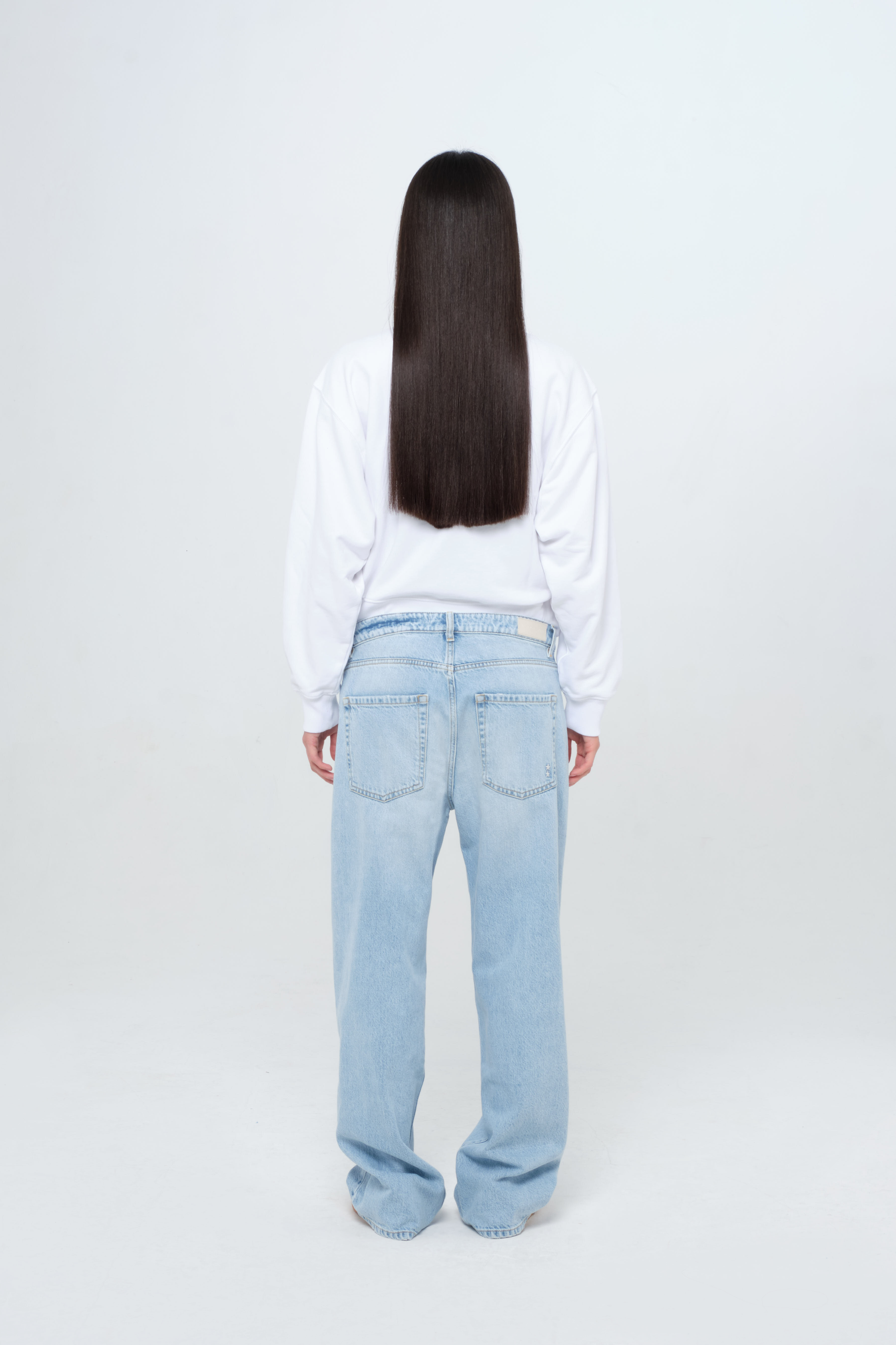 Back view of Bea women’s wide leg jeans in light wash, 100% rigid cotton denim, worn by a model with denim top and white jersey.