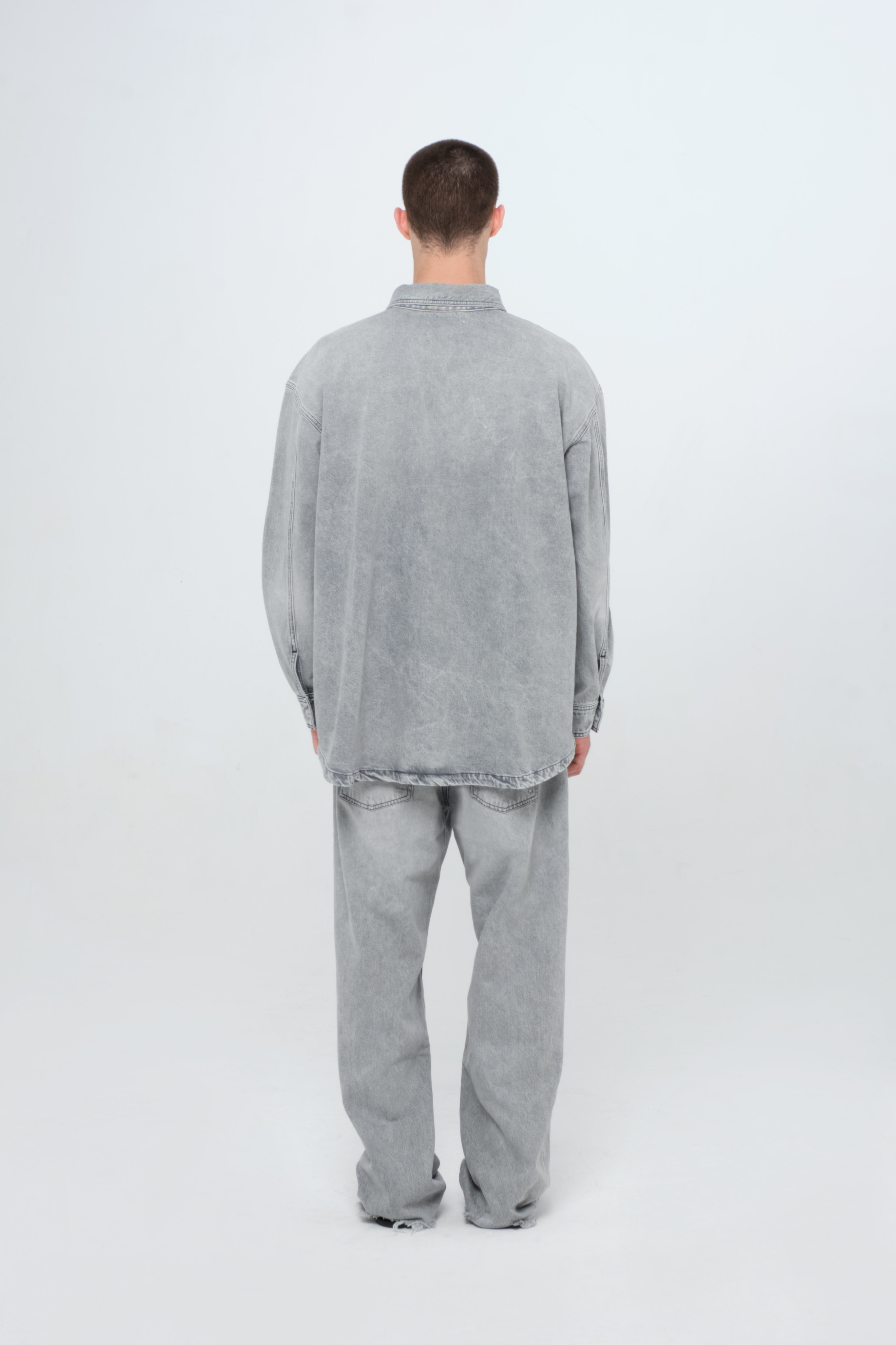 Back view of Billy men’s oversize shirt in gray wash, 100% rigid cotton denim, worn by a model with jeans.