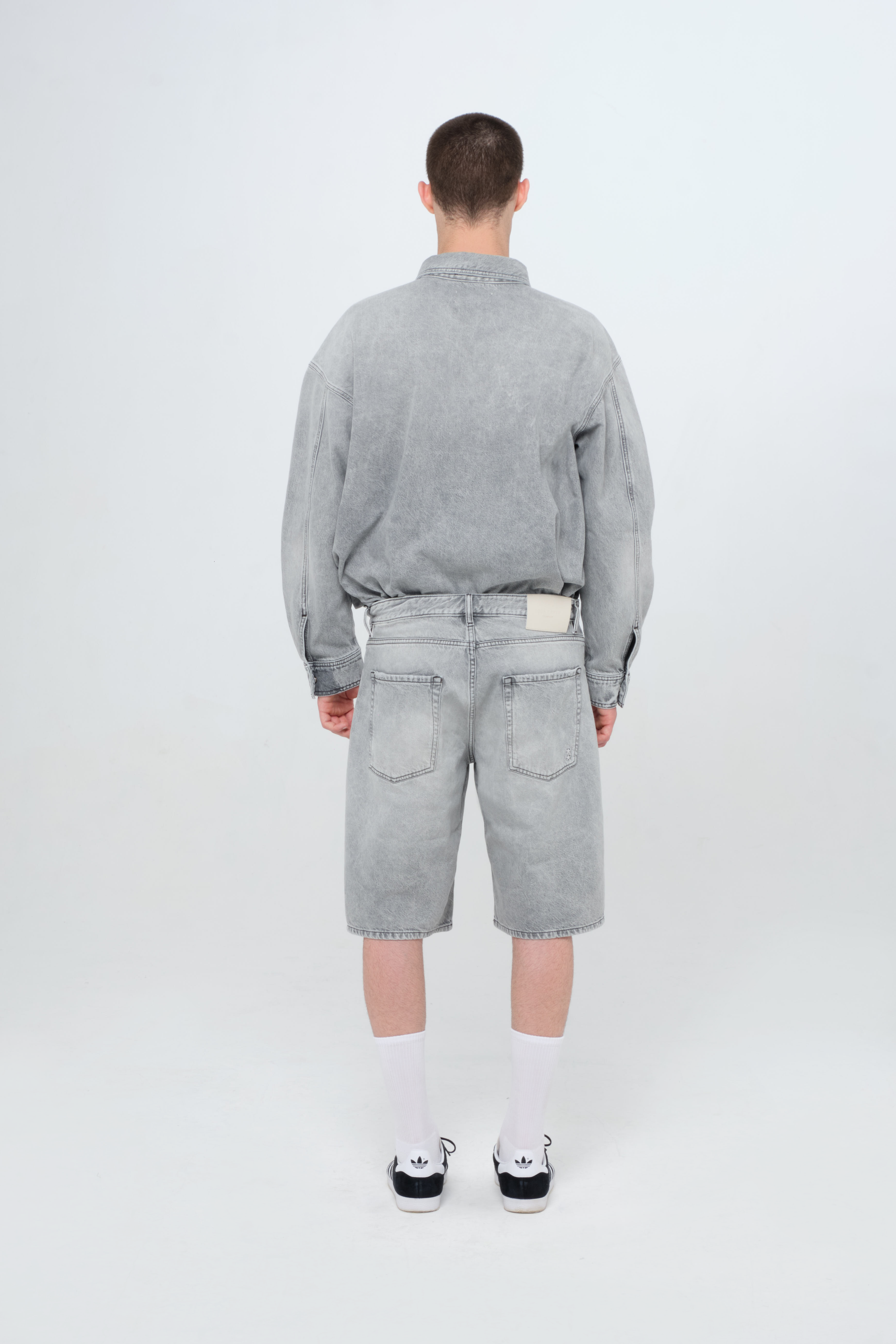 Back view of Bobby men’s short jeans in gray wash, 100% rigid cotton denim, worn by a model with a denim shirt.