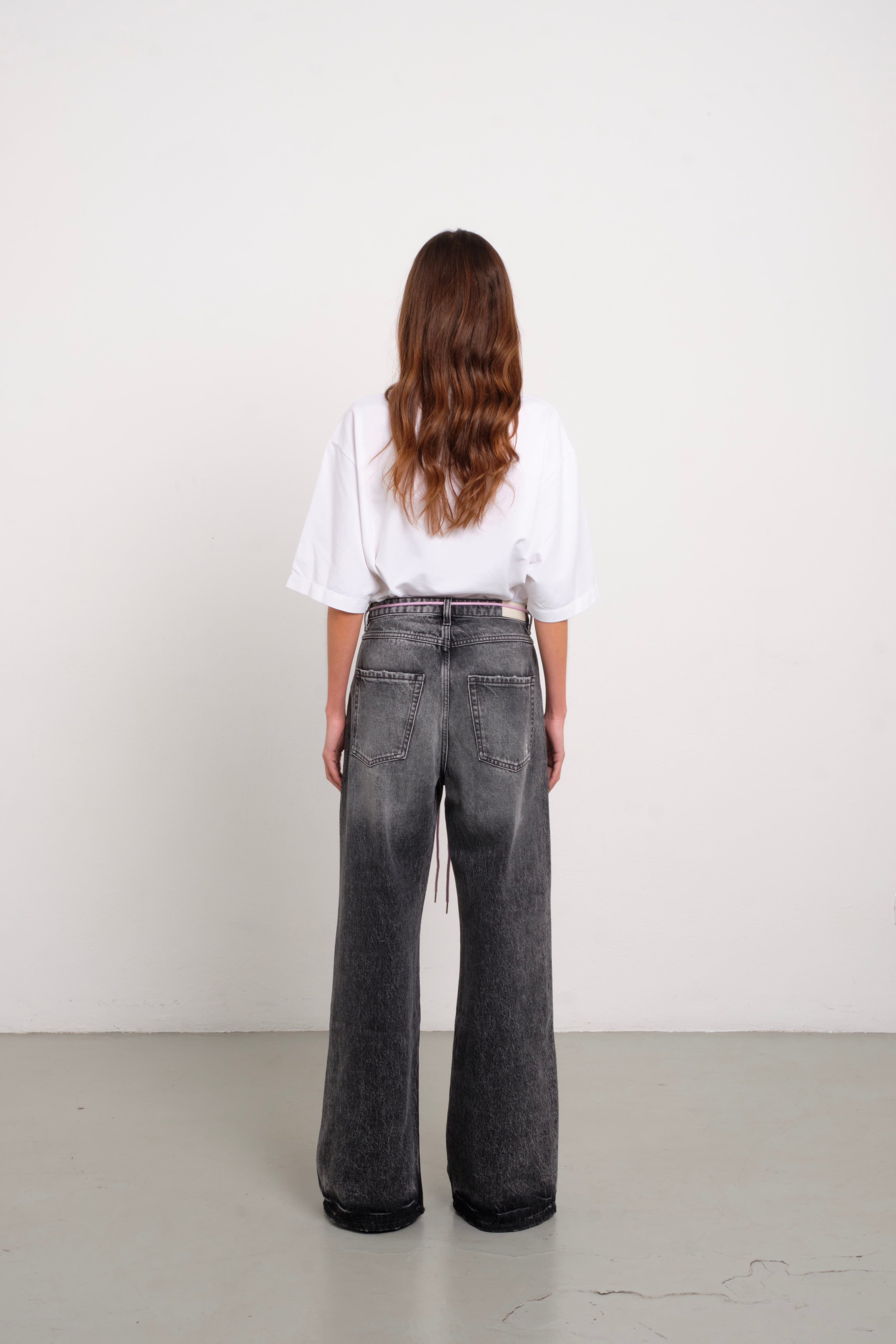 Back view of Debby women’s wide leg jeans in dark gray wash, 100% rigid cotton denim, worn by a model with a white shirt.