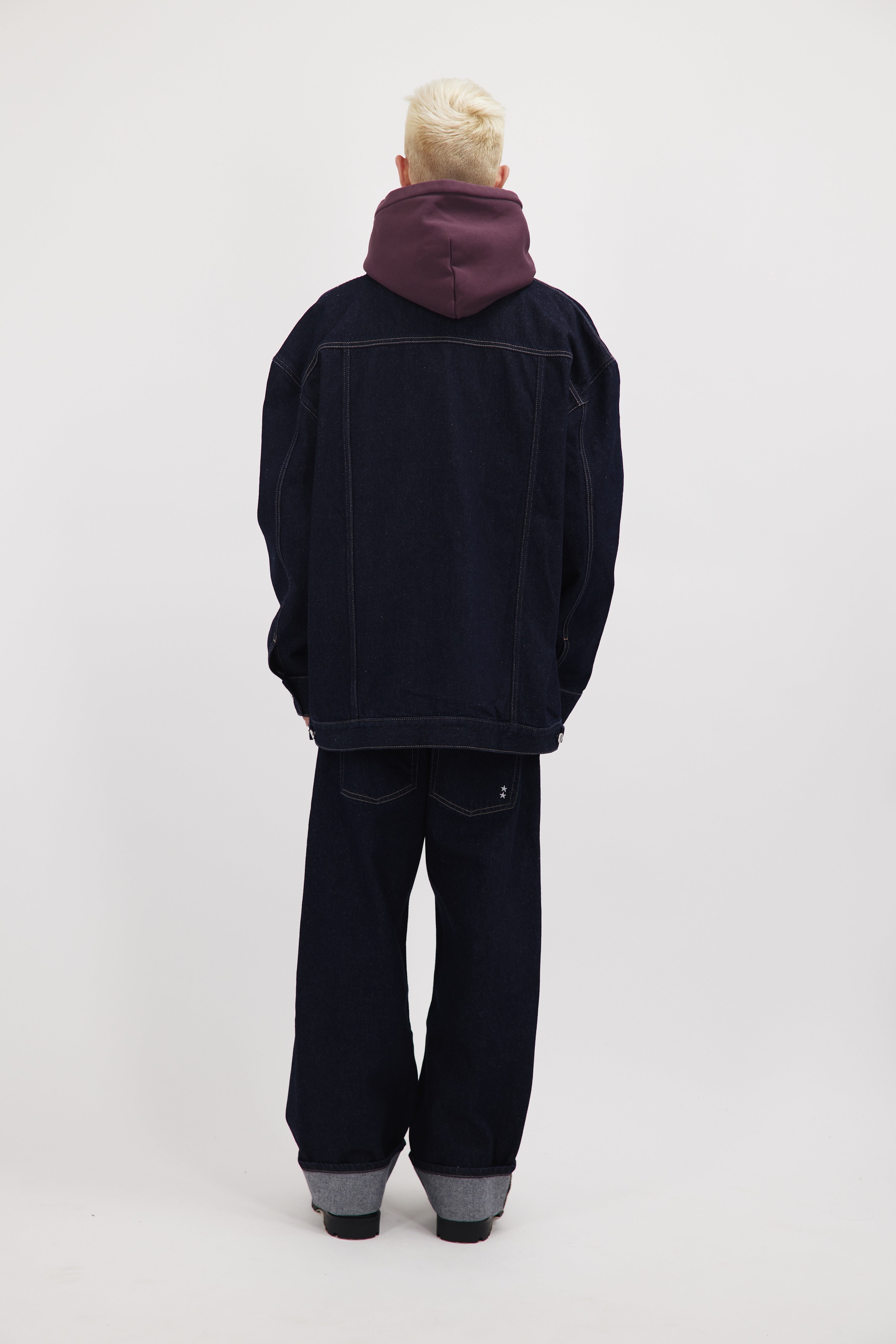 Back view of Drew men’s oversize jacket in indigo raw, 100% rigid cotton denim, worn by a model with jeans.
