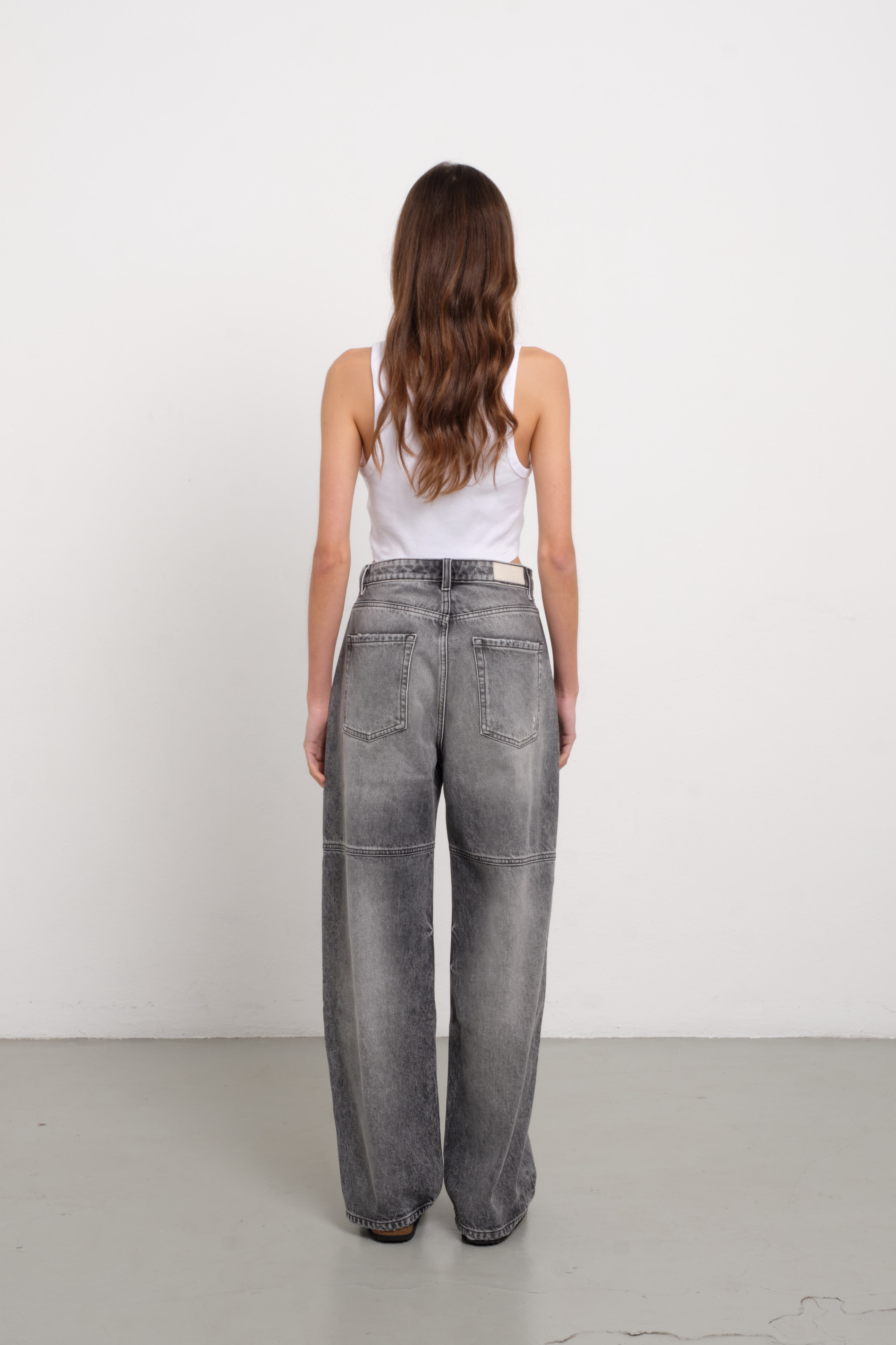Back view of Jenny women’s straight leg jeans in dark gray wash, 100% rigid cotton denim, worn by a model with a blue tank top.