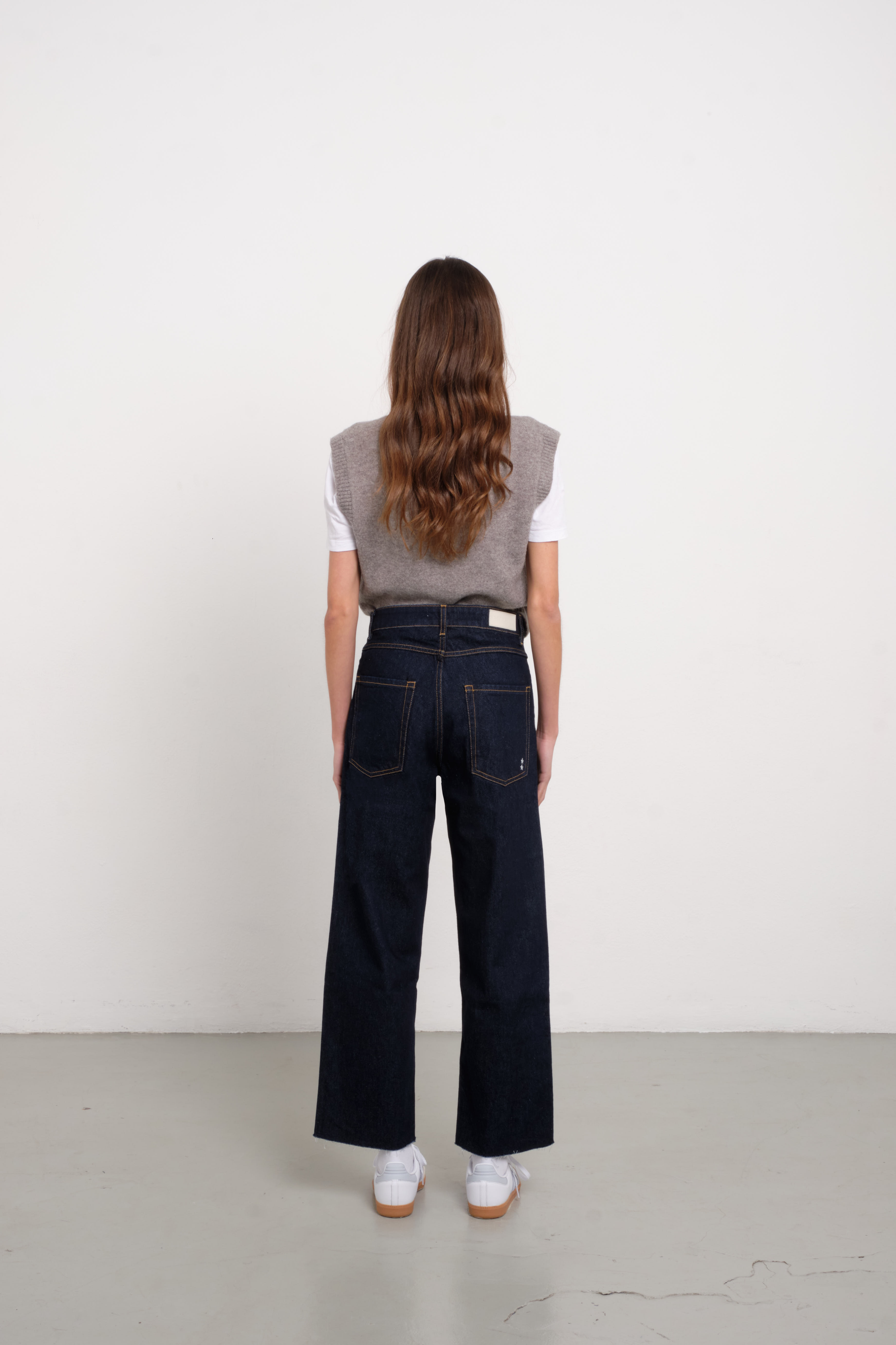 Back view of Jill women’s straight leg jeans in indigo raw, 100% rigid cotton denim, worn by a model with a white shirt.