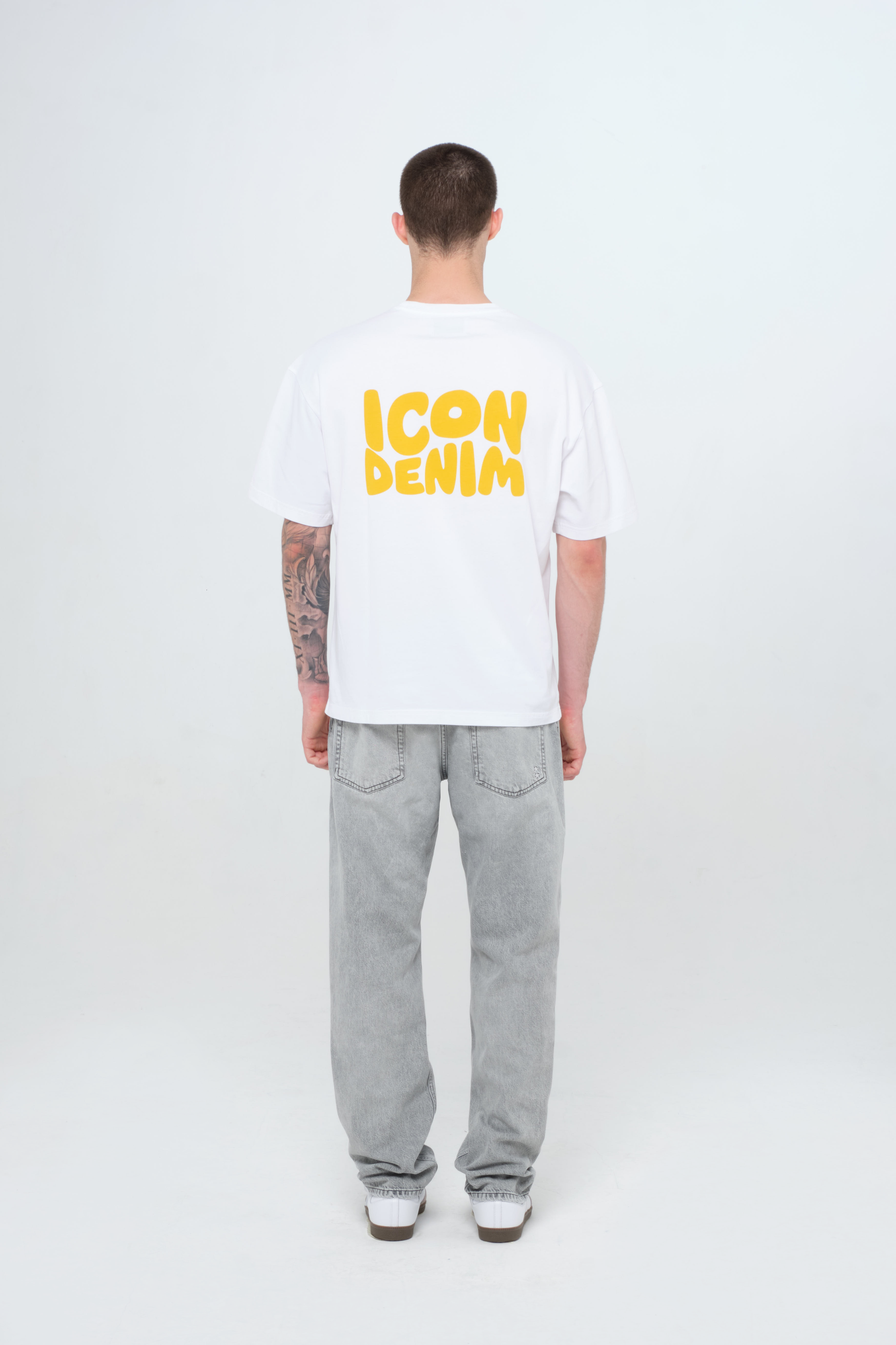 Back view of Kanye men’s loose jeans in gray wash, 100% rigid cotton denim, worn by a model with a white t-shirt.