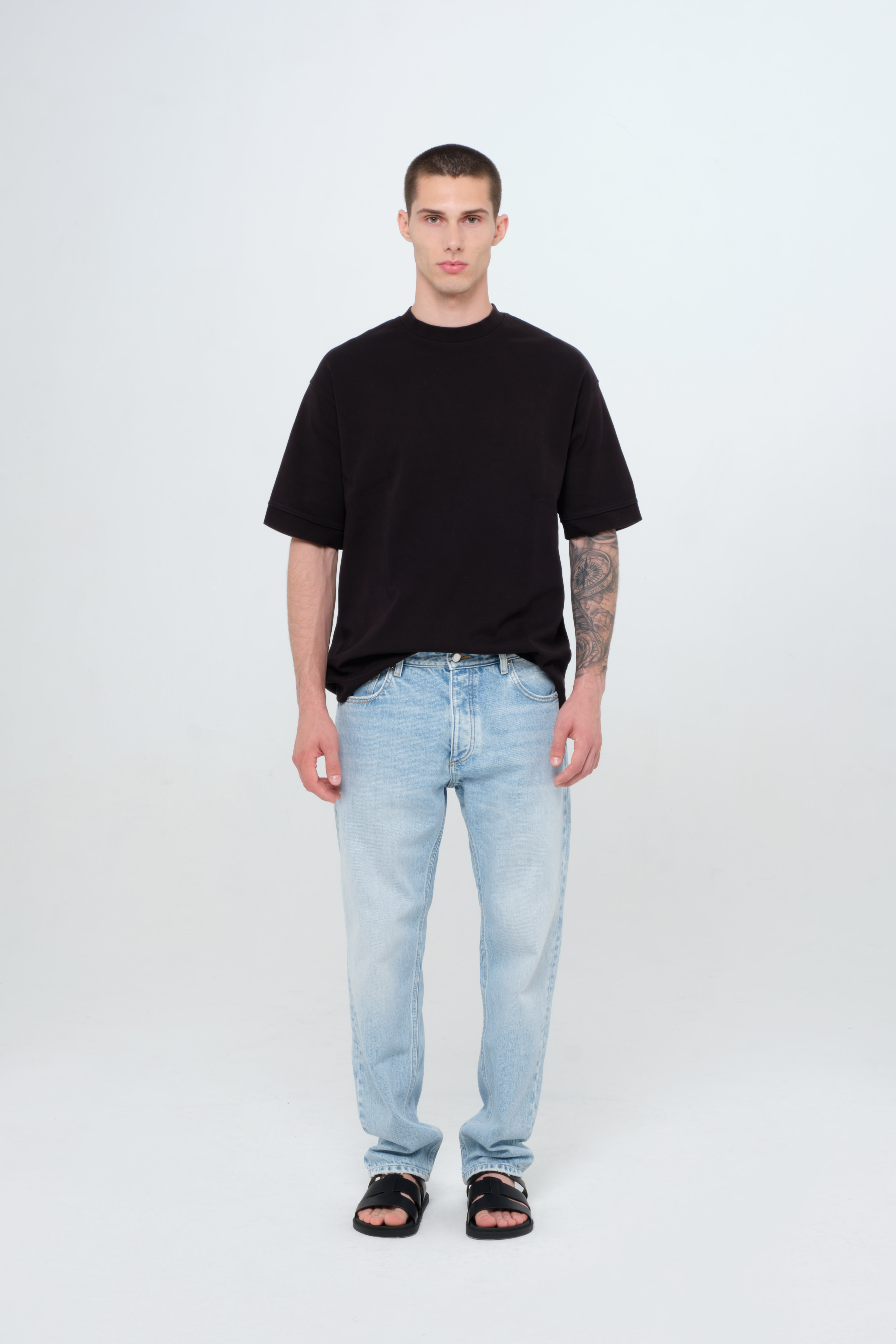 Kanye men’s loose jeans in light wash, 100% rigid cotton denim, worn by a model with a black t-shirt.