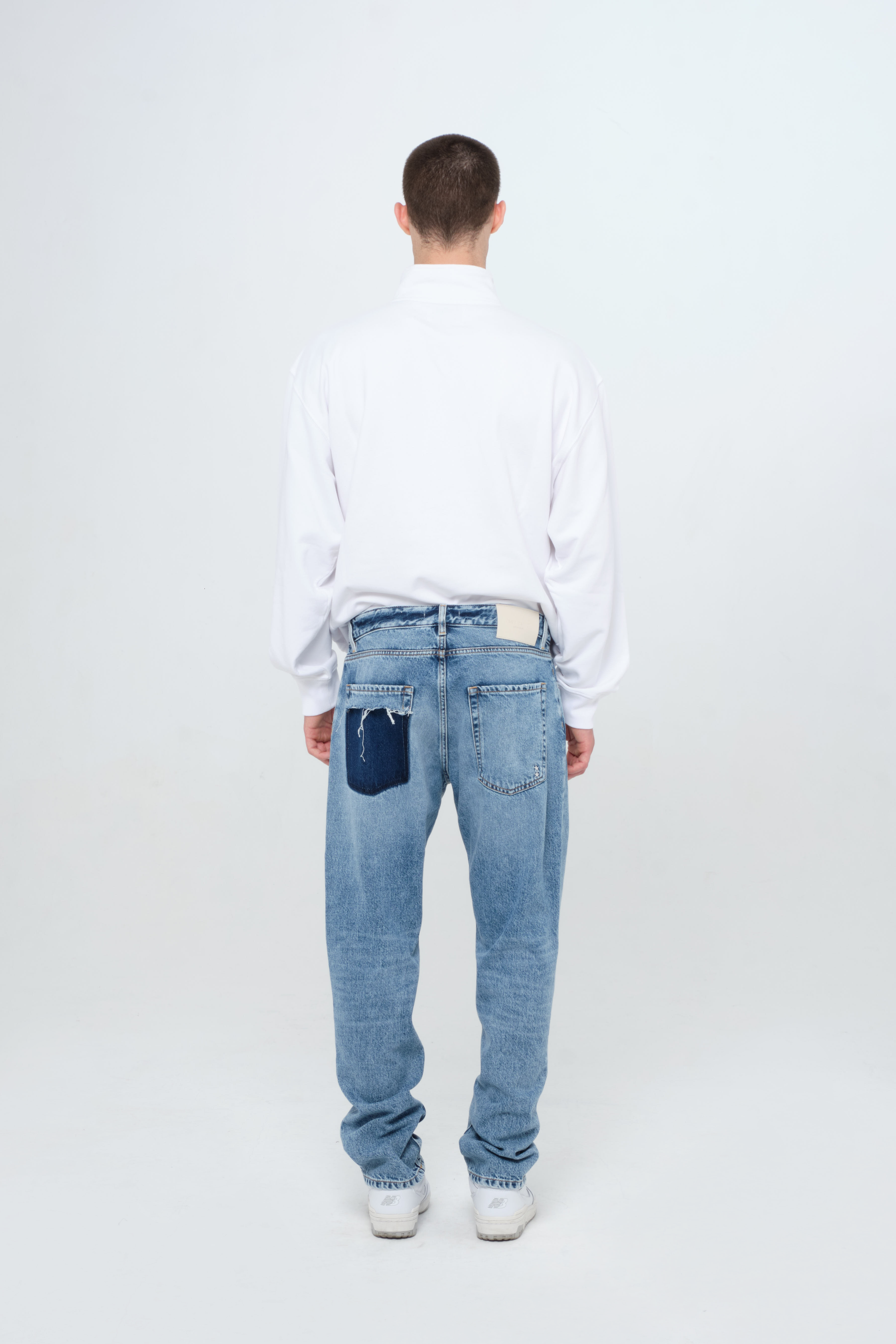 Back view of Kanye men’s loose jeans in medium wash, 100% rigid cotton denim, worn by a model with a white sweatshirt.