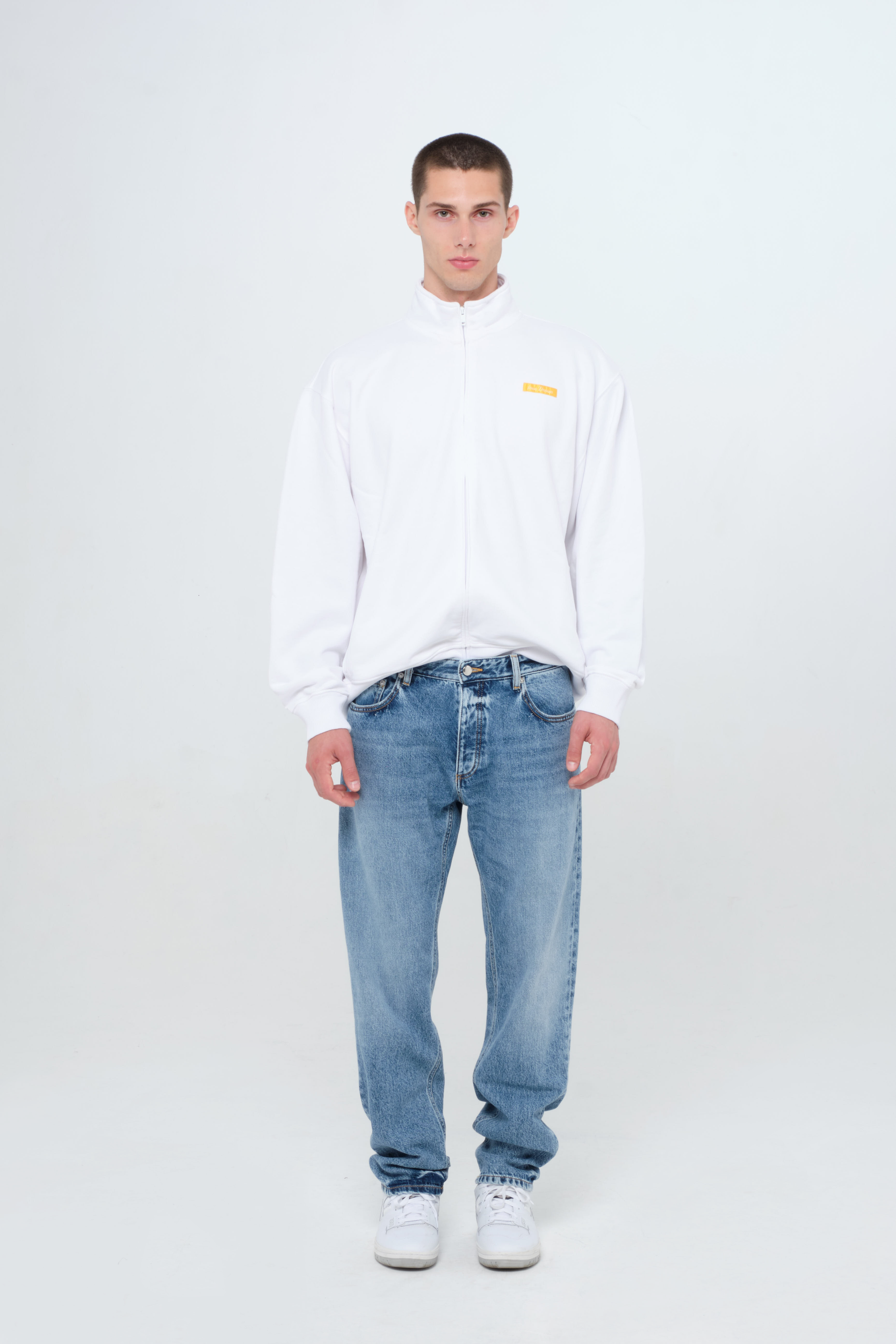 Kanye men’s loose jeans in medium wash, 100% rigid cotton denim, worn by a model with a white sweatshirt.