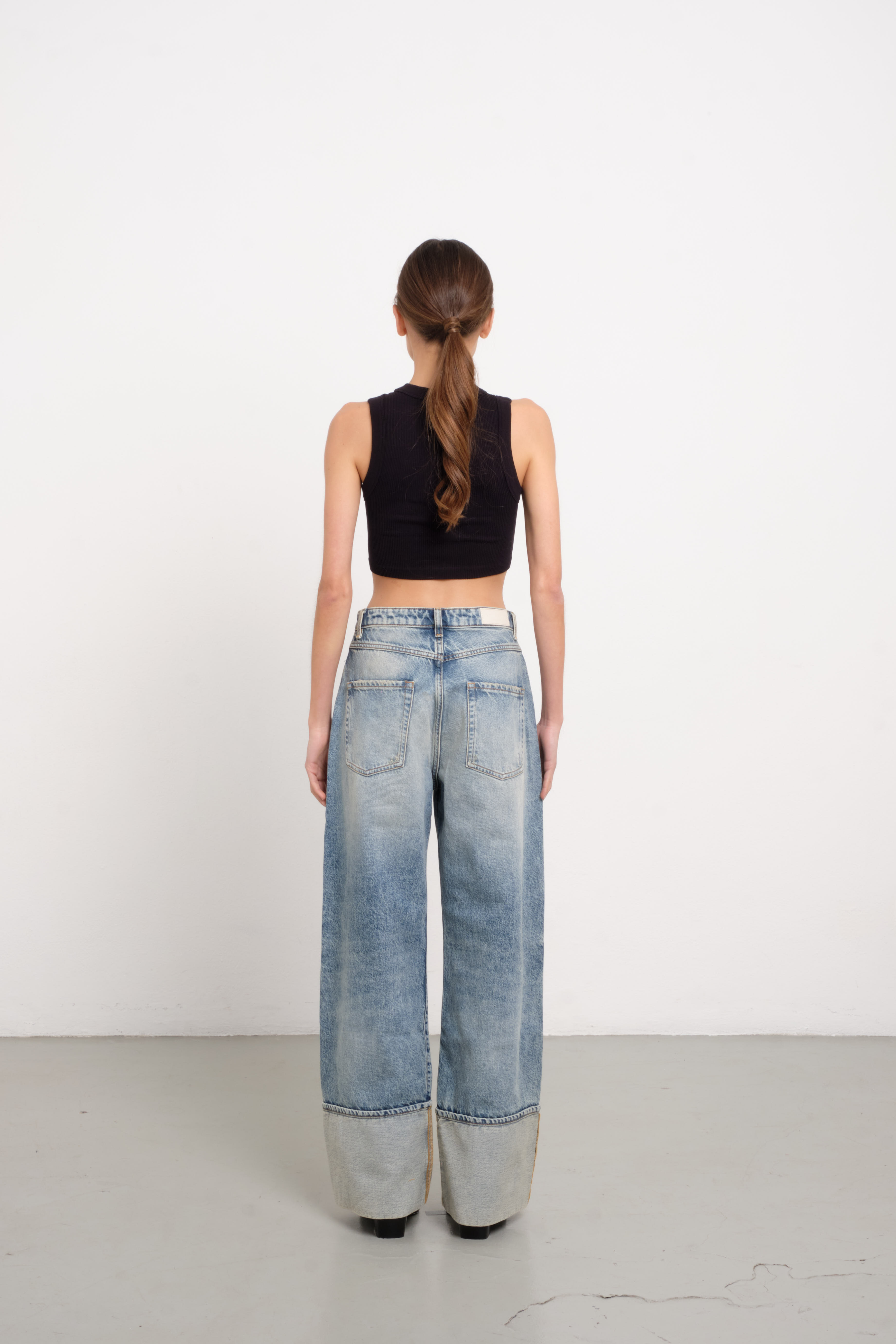 Back view of Kiki women’s wide leg jeans in old effect wash, 100% rigid cotton denim, worn by a model with a black top.