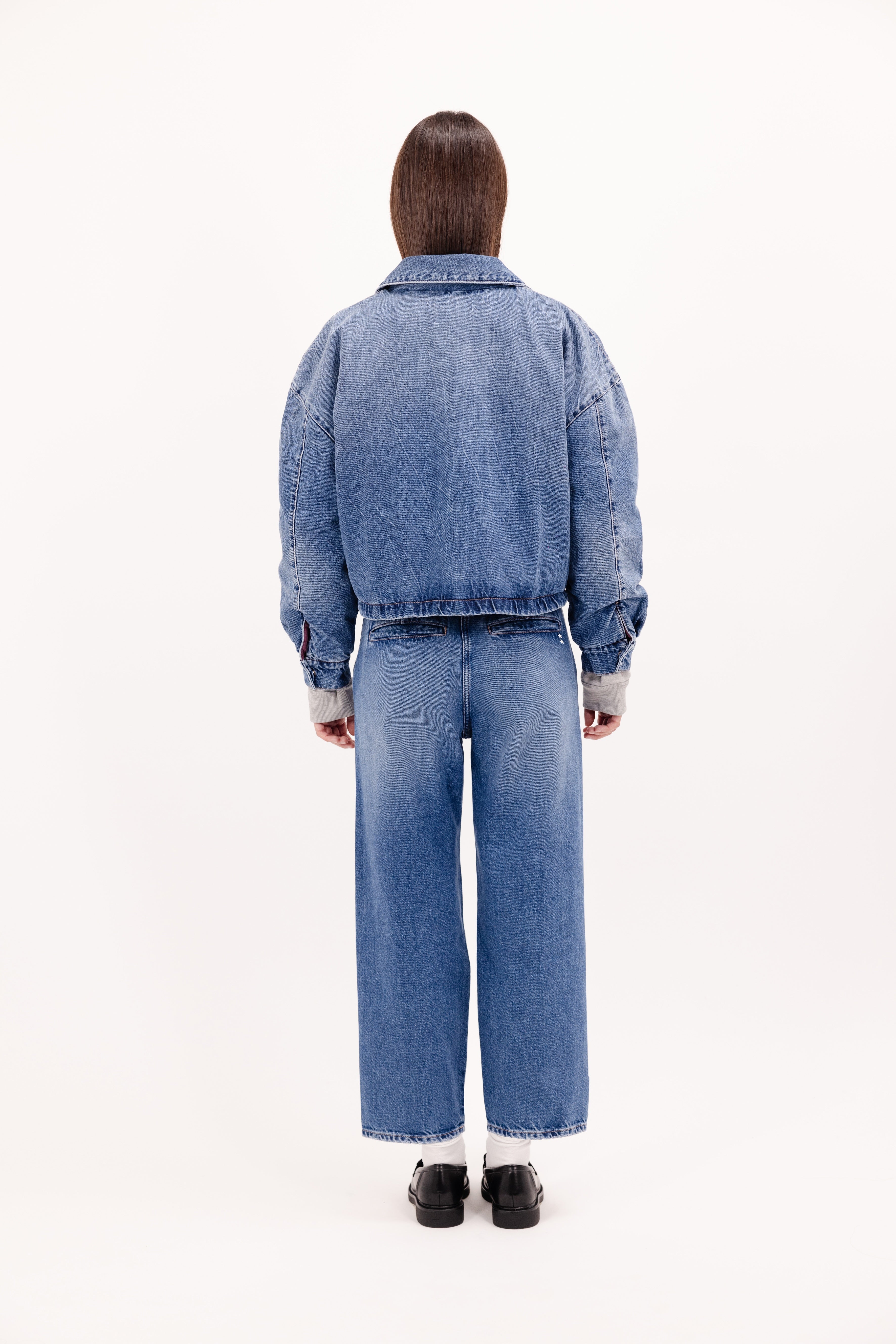 Back view of Kleo women’s jacket in eclipse wash, 100% rigid cotton denim, worn by a model with jeans.