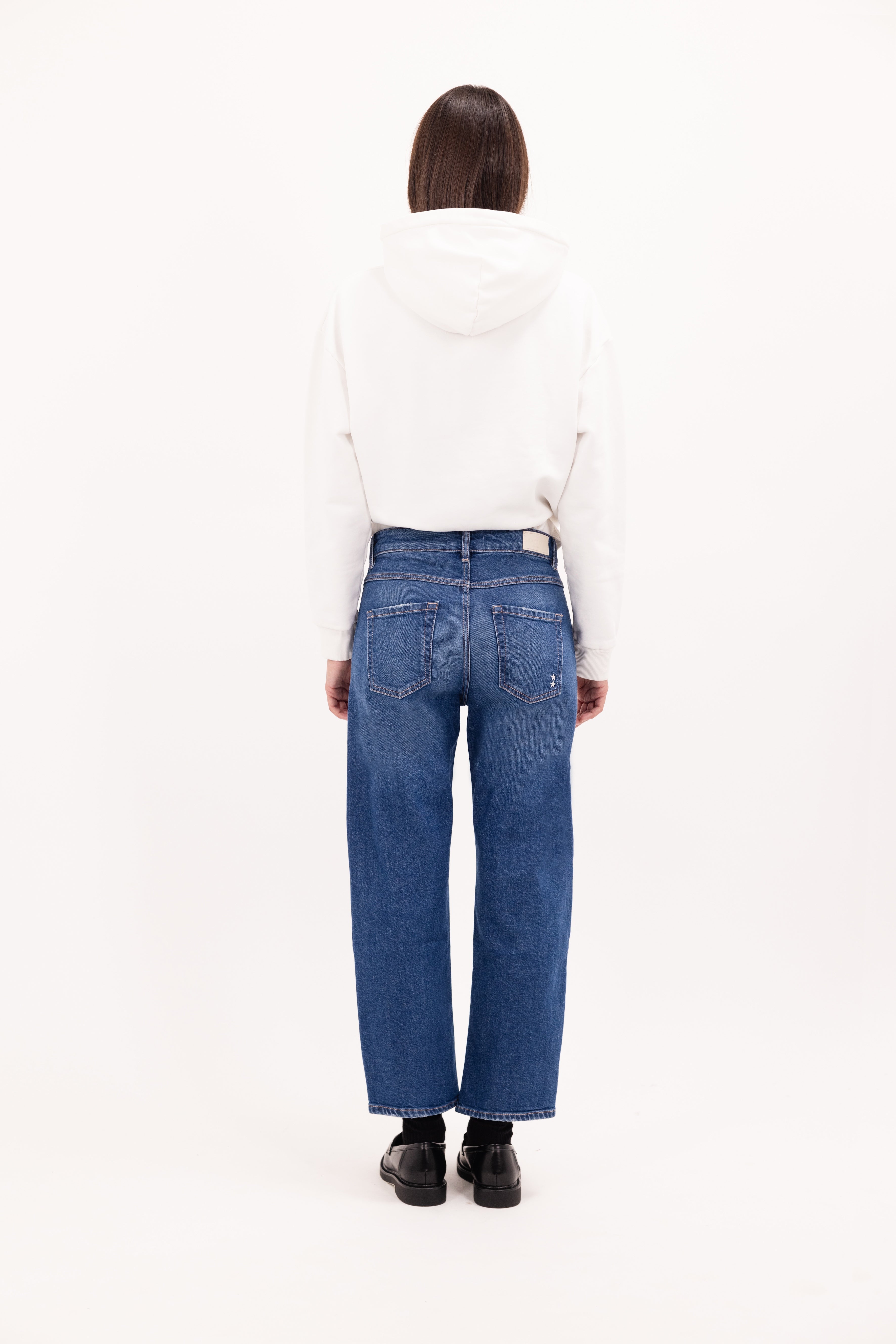 Back view of Mimi women’s straight leg jeans in dusty blue wash, 99% cotton denim and 1% elastan fibers, worn by a model with a white sweatshirt.