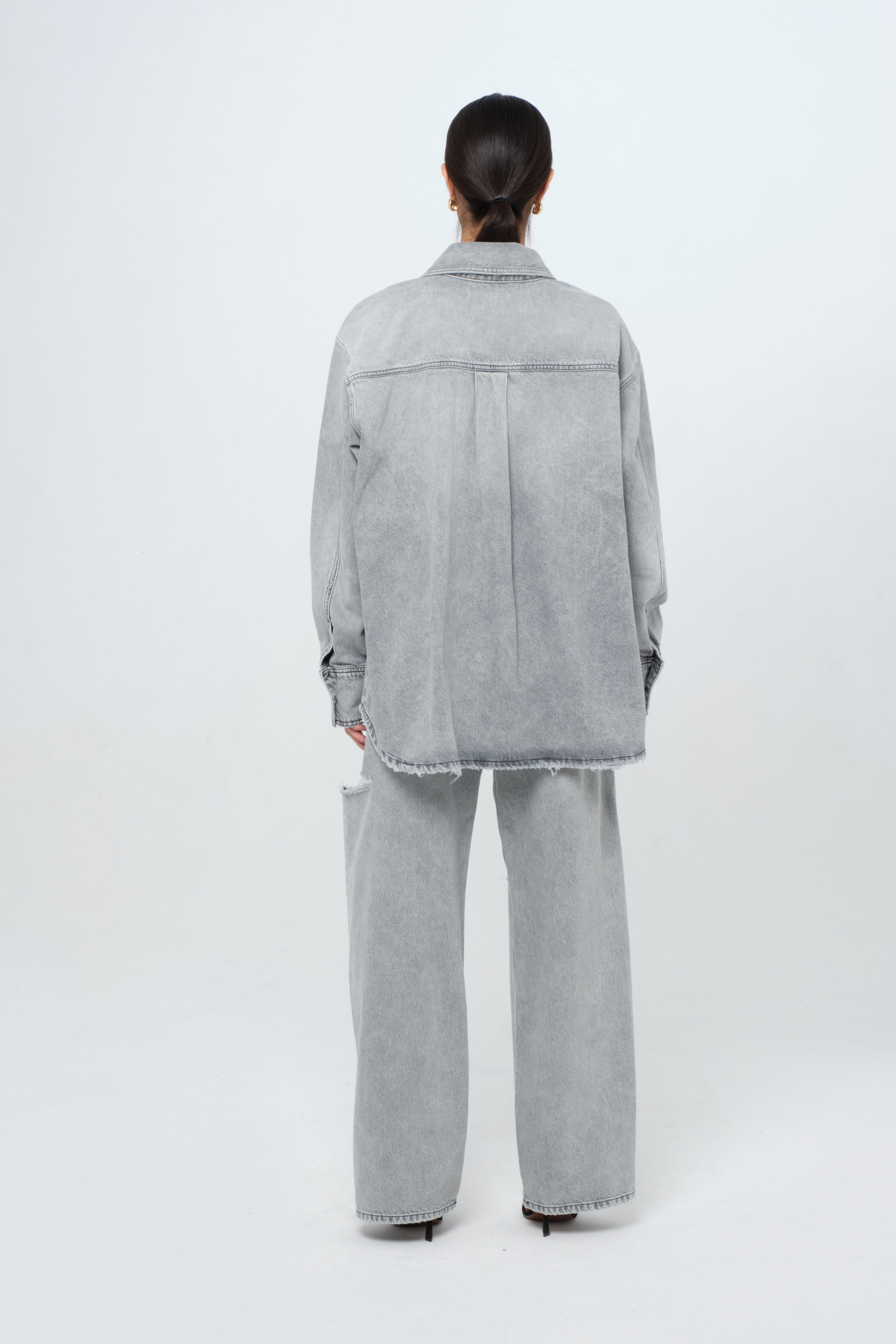 Back view of Noa women’s oversize shirt in gray wash, 100% rigid cotton denim, worn by a model with jeans.