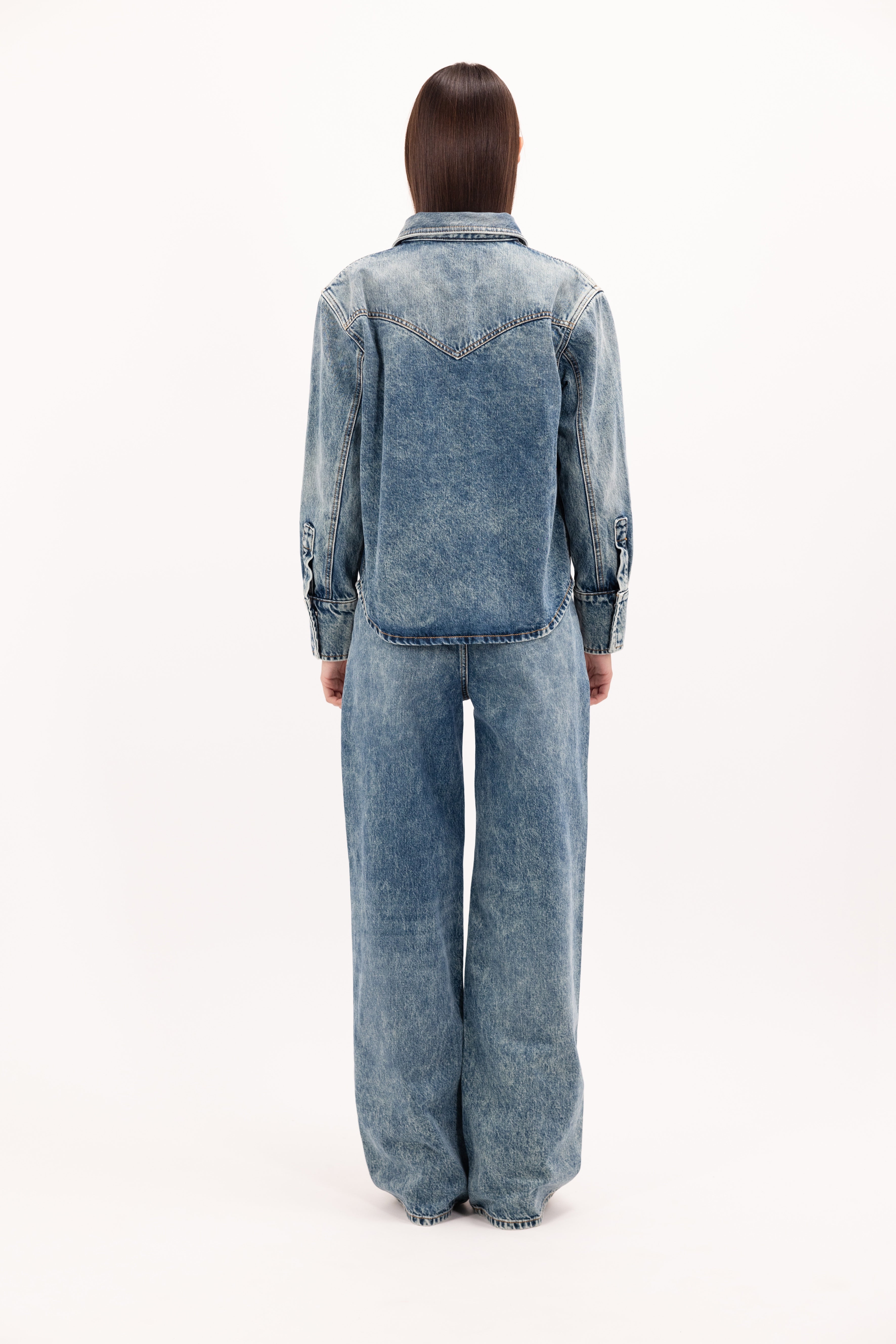 Back view of Norah women’s regular shirt in aged stone wash, 100% rigid cotton denim, worn by a model wide jeans.