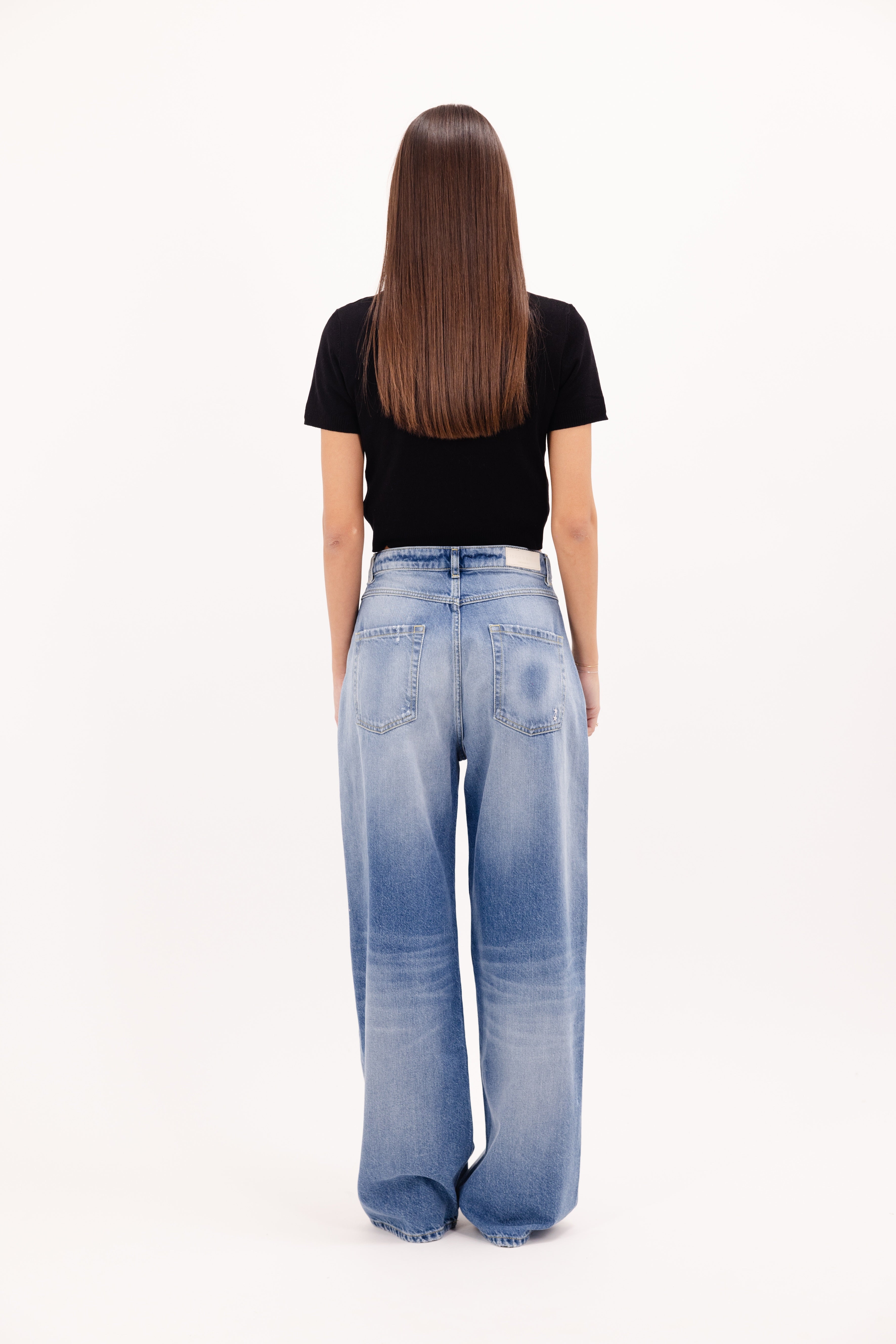Back view of Poppy women’s wide leg jeans in misty blue wash, 100% rigid cotton denim, worn by a model with a black top.