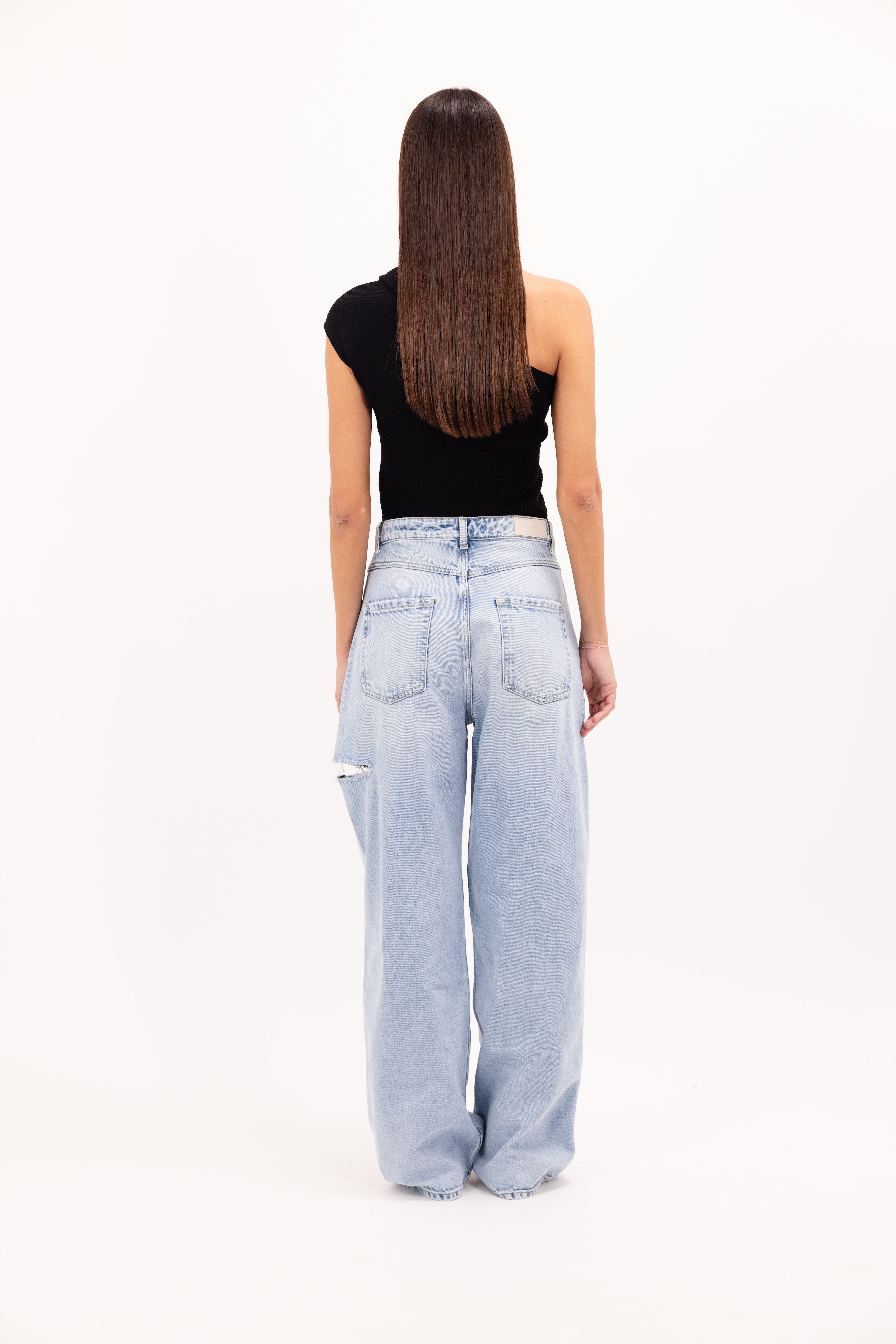 Back view of Poppy women’s wide leg jeans in sky blue wash, 100% rigid cotton denim, worn by a model with a black top.