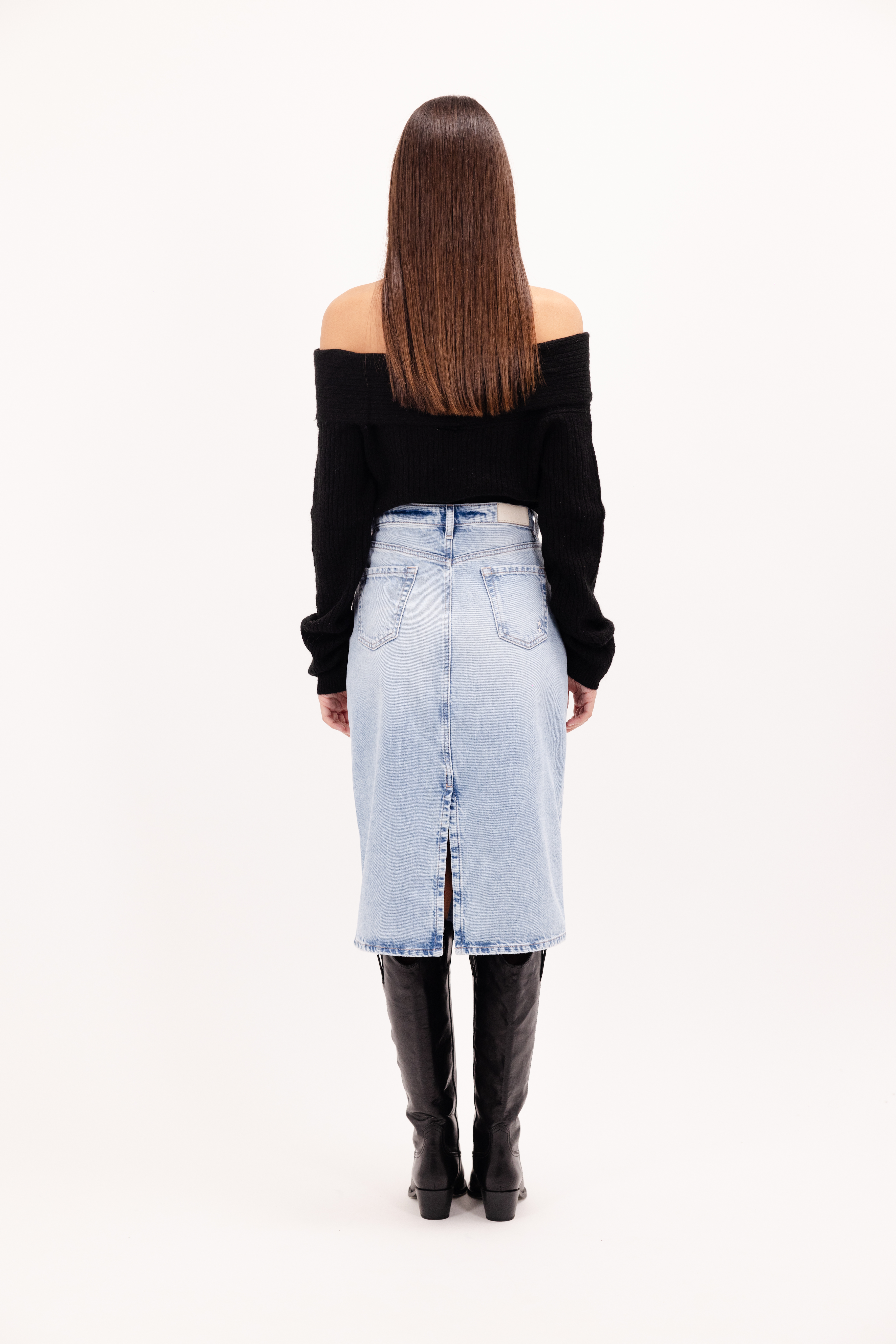 Back view of Ruby women’s midi skirt in sky blue wash, 100% rigid cotton denim, worn by a model with a black top.