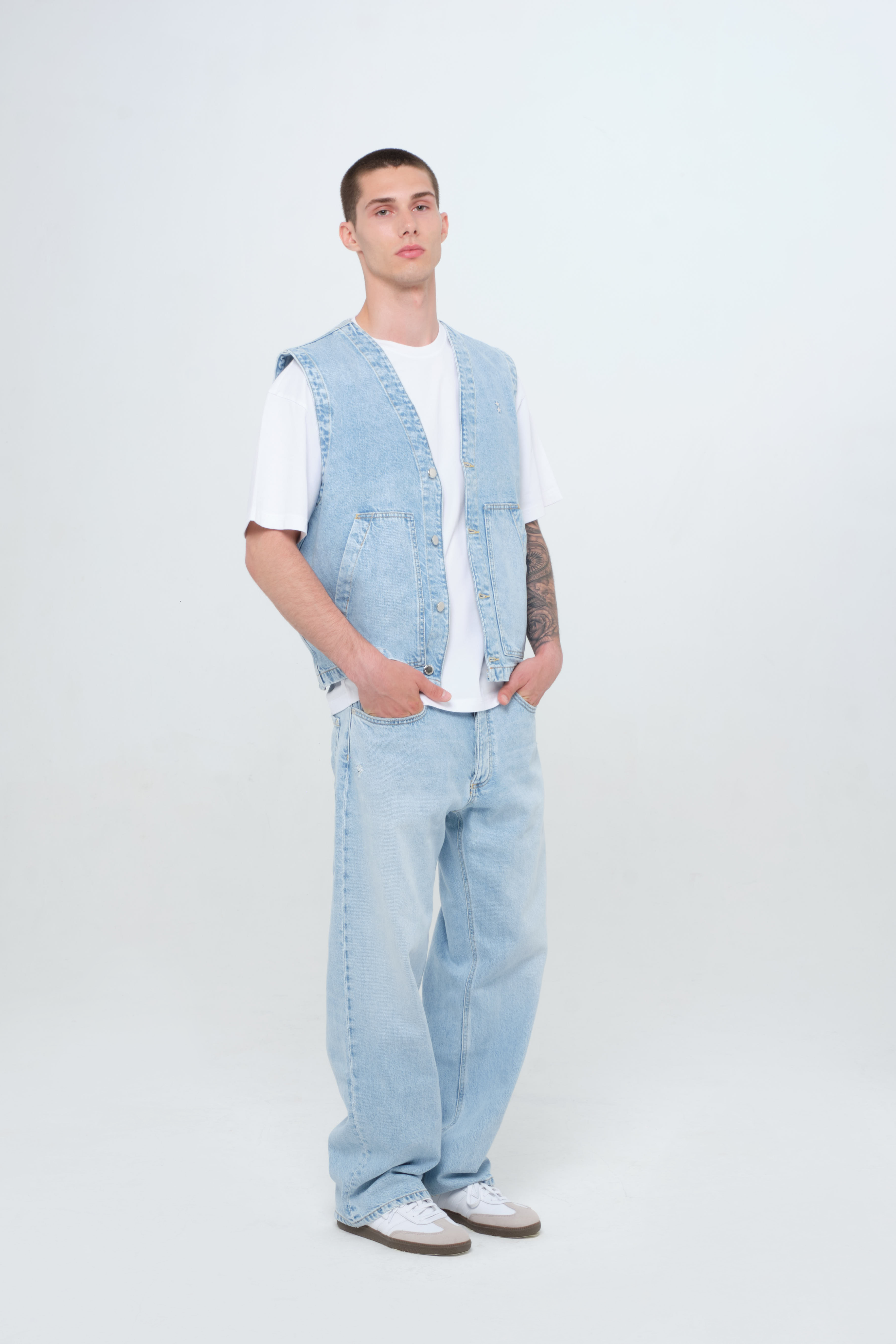 Will men’s wide leg jeans in light wash, 100% rigid cotton denim, worn by a model with a denim vest.