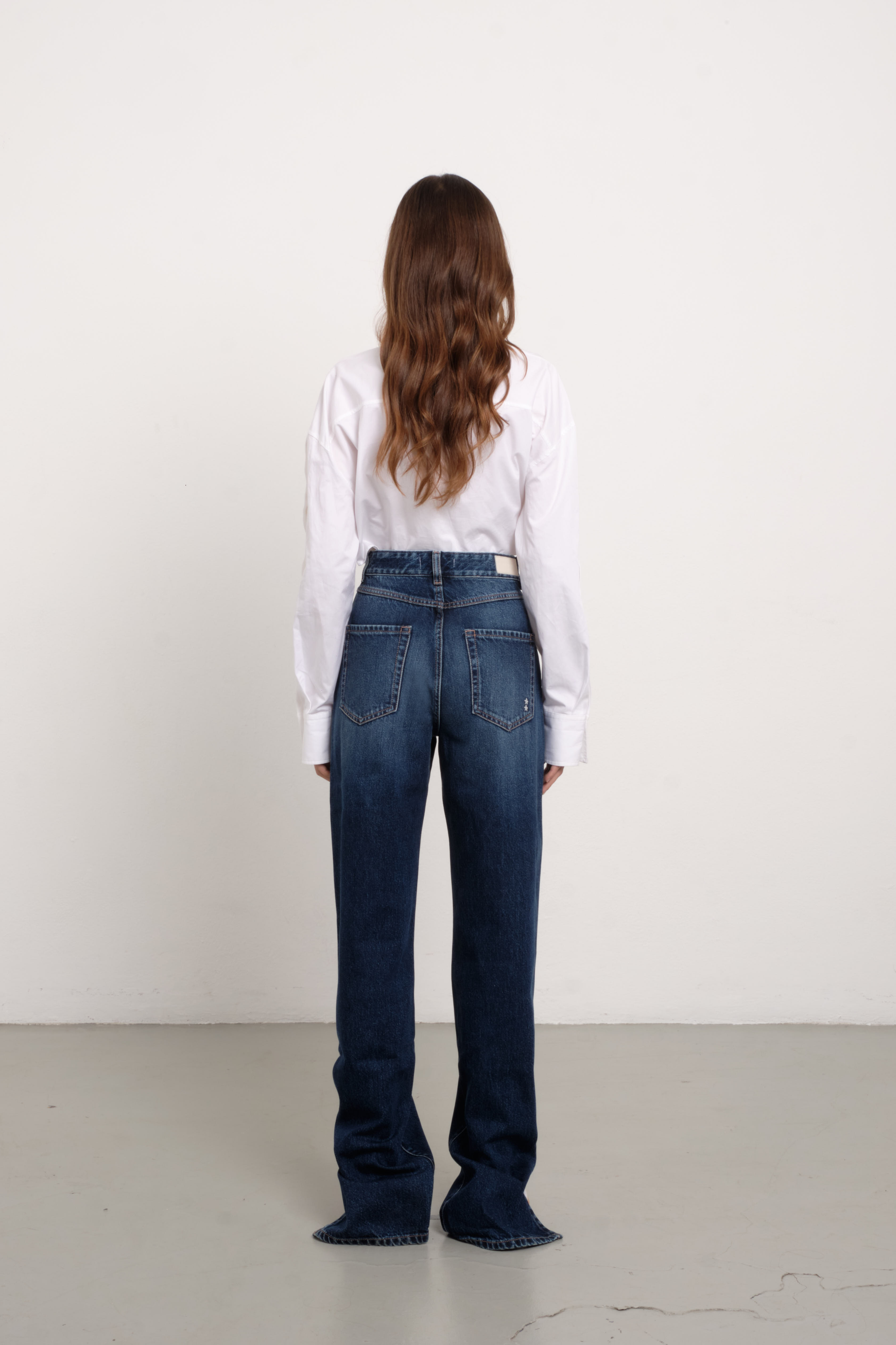 Back view of Jodie women’s straight leg jeans in dark wash, 100% rigid cotton denim, worn by a model with a white shirt.
