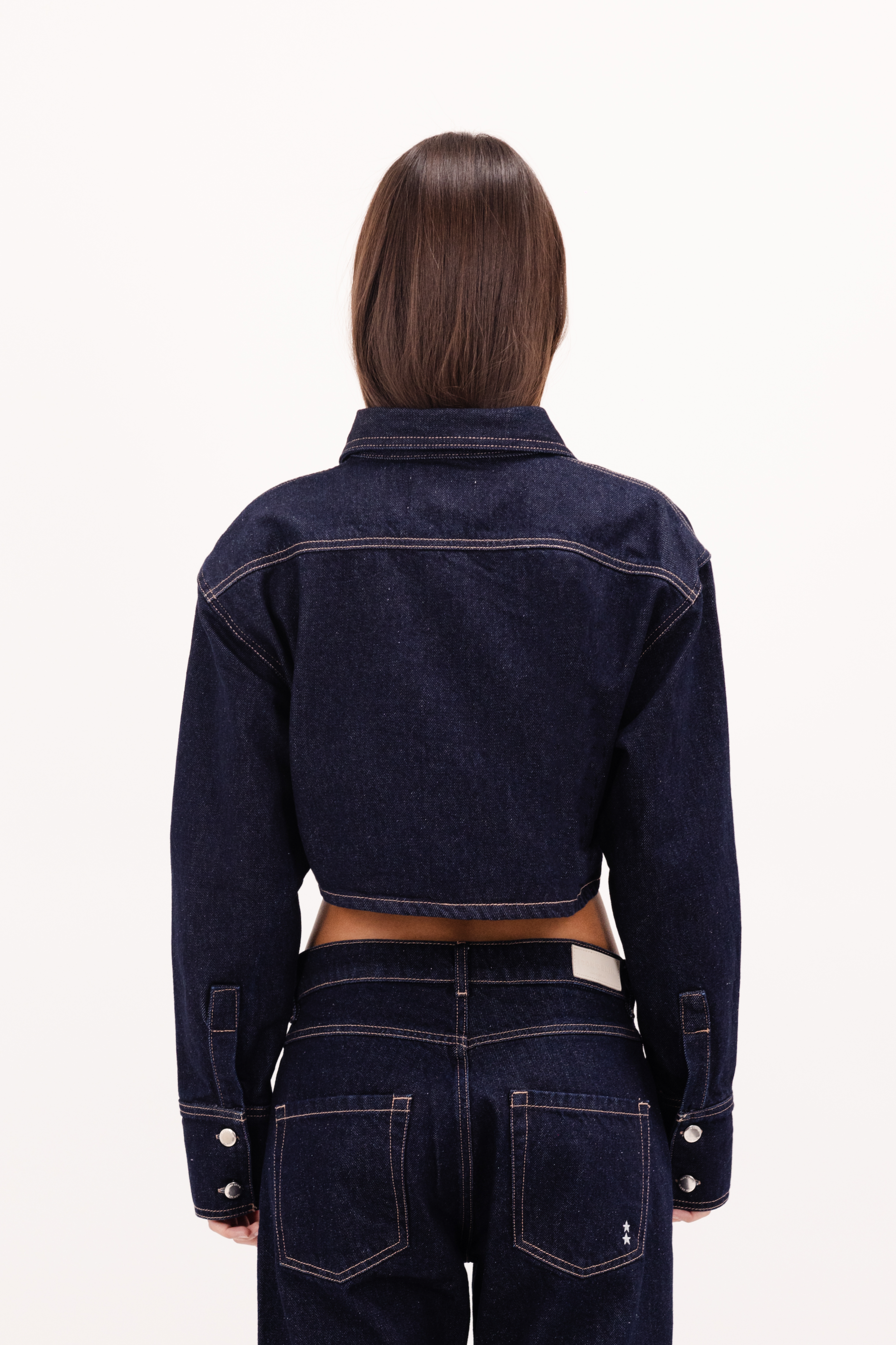 Back view of Amber women’s denim shirt in indigo raw, 100% rigid cotton denim, worn by a model with a denim jeans.
