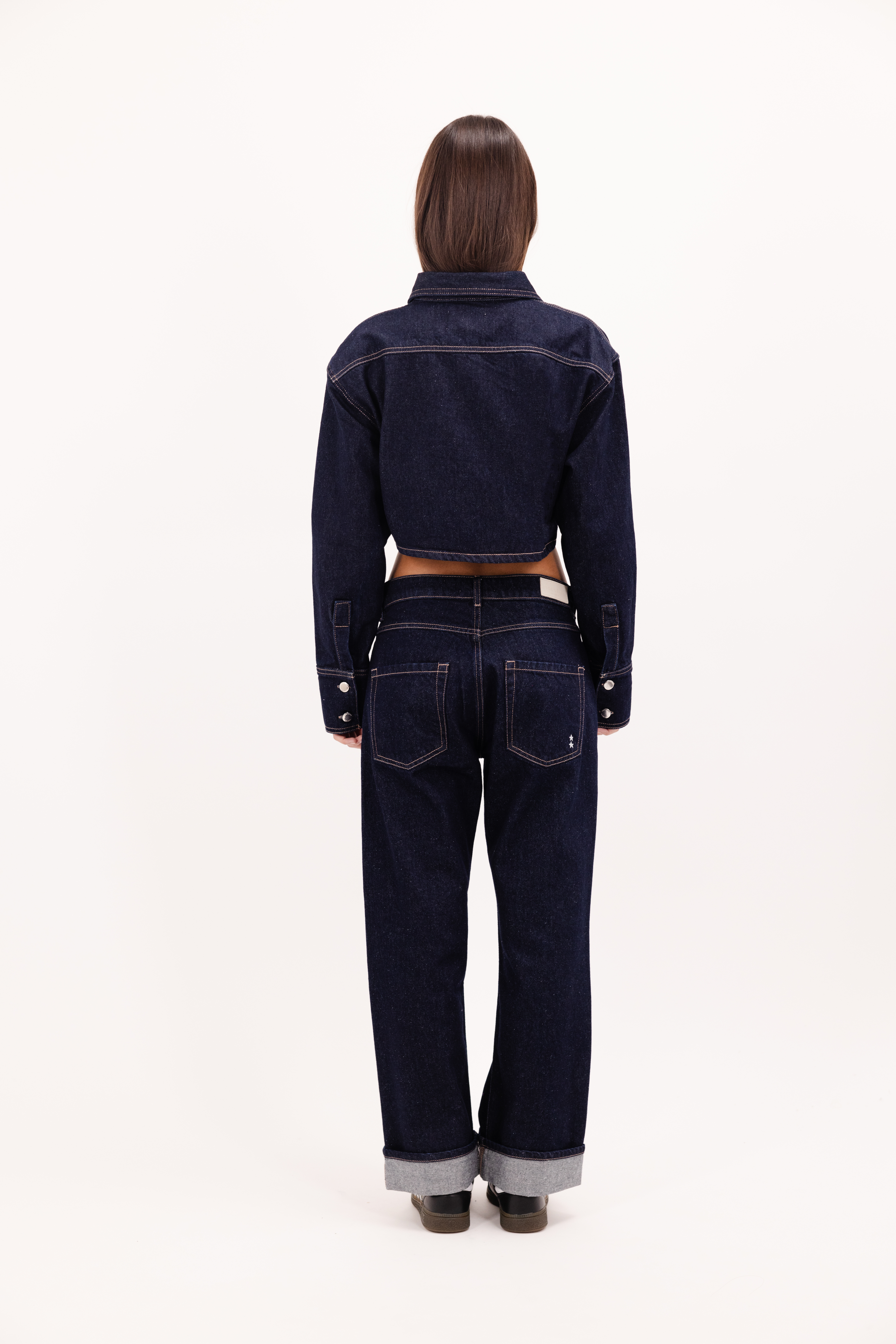 Back view of Amber women’s denim shirt in indigo raw, 100% rigid cotton denim, worn by a model with a denim jeans.

