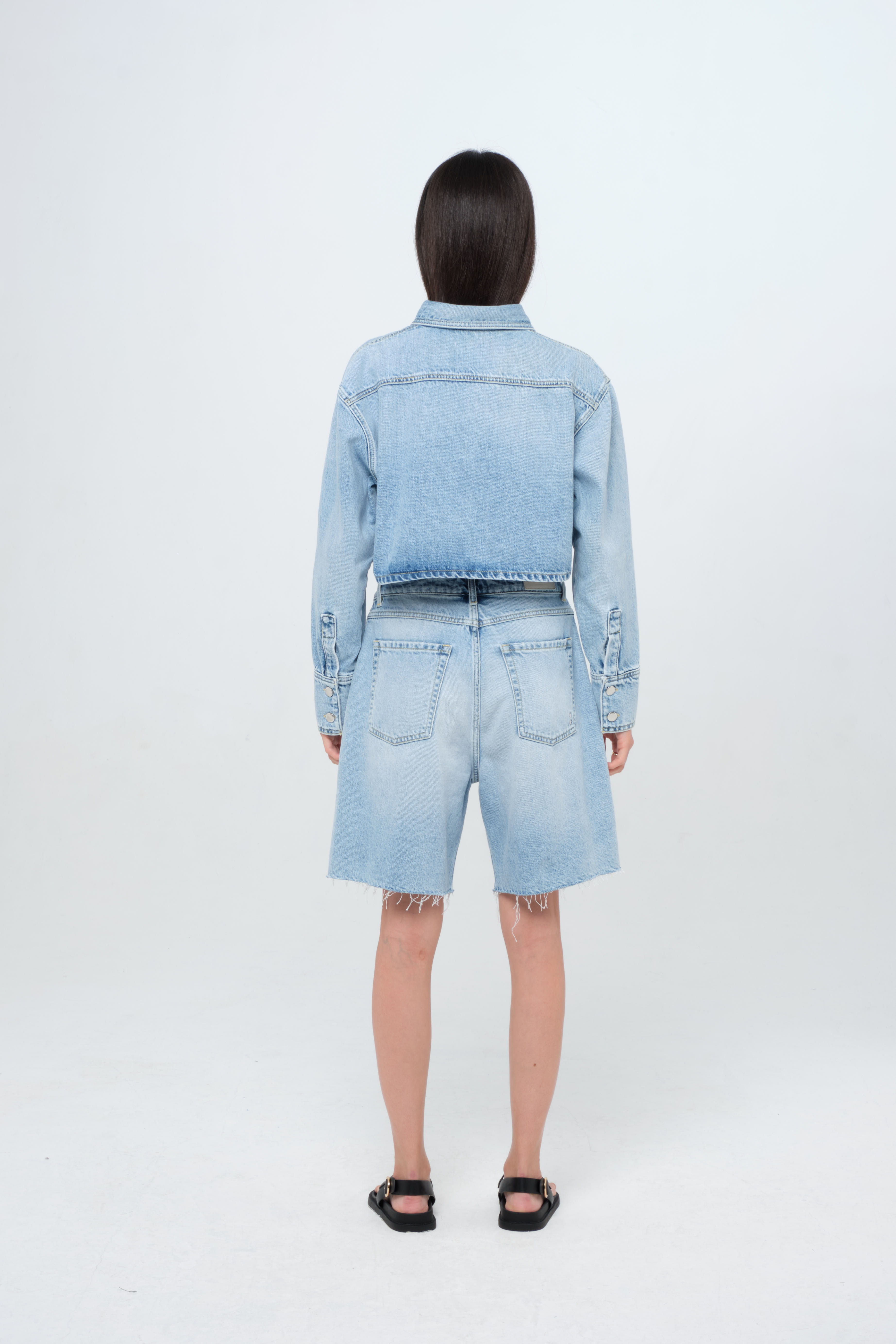 Back view of Amber women’s denim shirt in light wash, 100% rigid cotton denim, worn by a model with a denim short.
