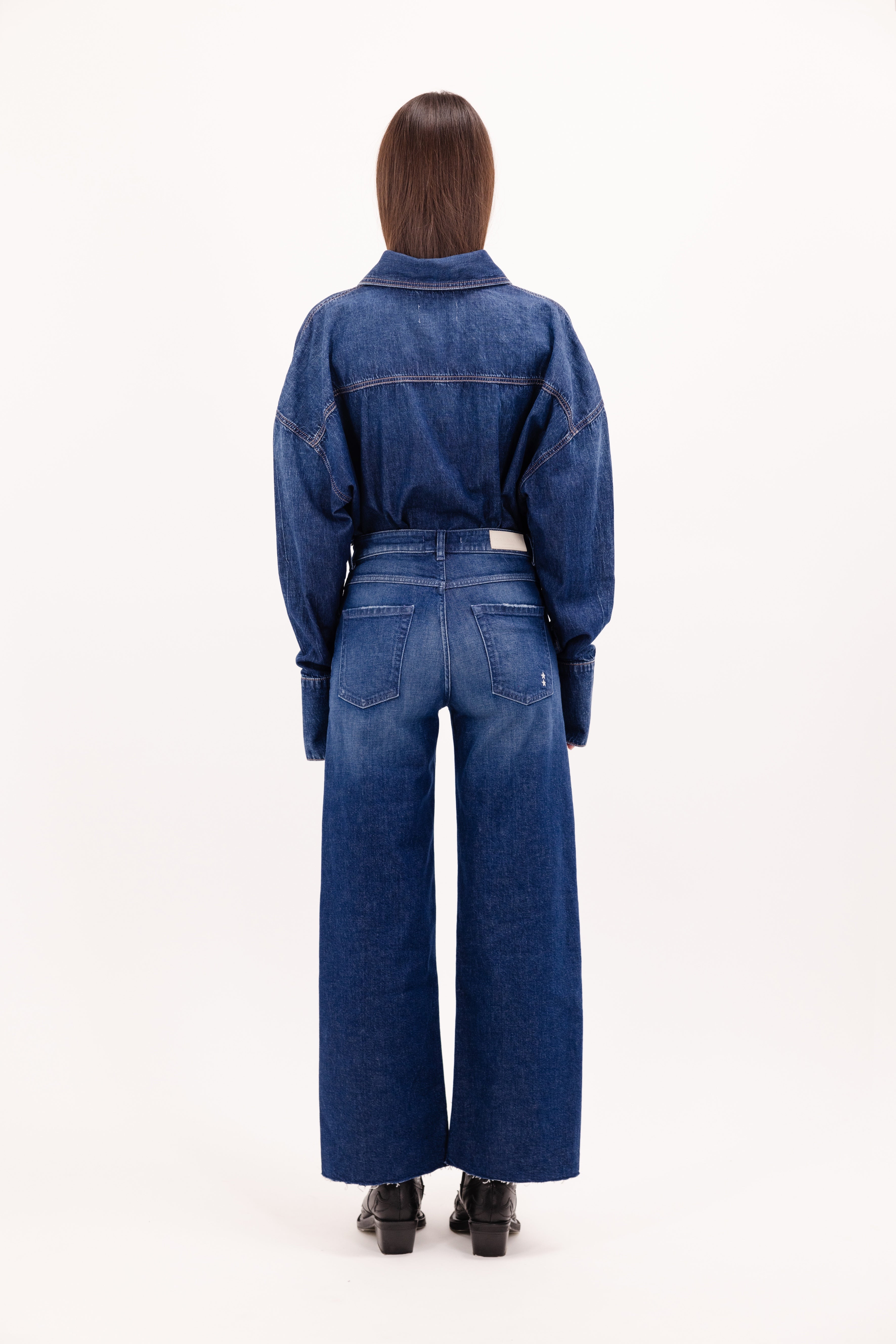 Back view of Angie women’s flared crop jeans in dusty blue wash, 99% cotton denim and 1% Elastan fibers, worn by a model with a denim shirt.