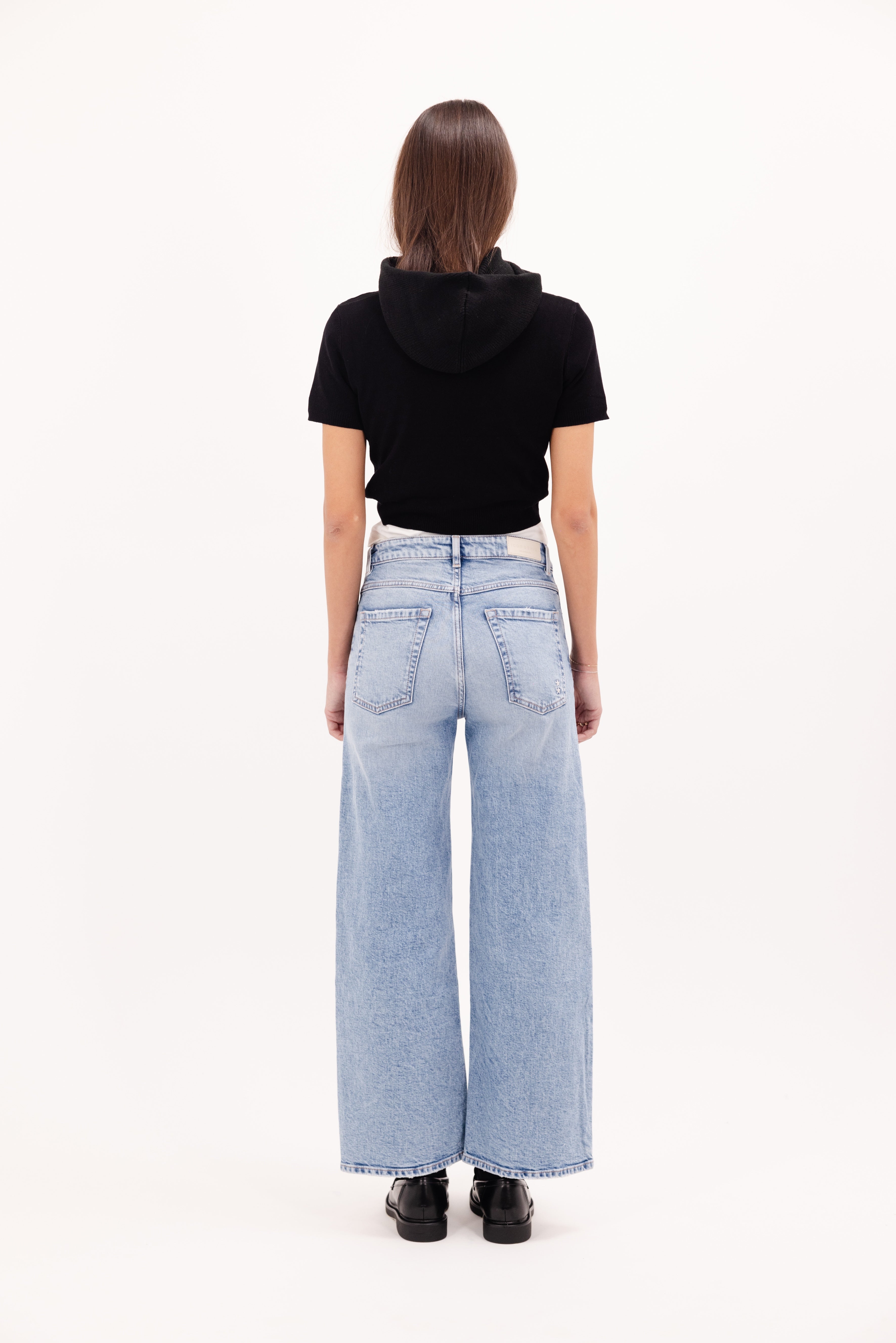 Back view of Angie women’s flared crop jeans in sky blue wash, 99% cotton denim and 1% Elastan fibers, worn by a model with a black top.
