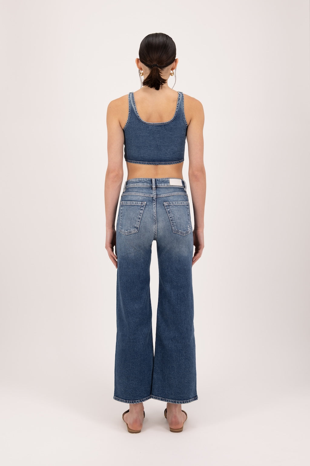 Back view of Angie women’s flared crop jeans in dark used wash, 99% cotton denim and 1% Elastan fibers, worn by a model with a denim top.