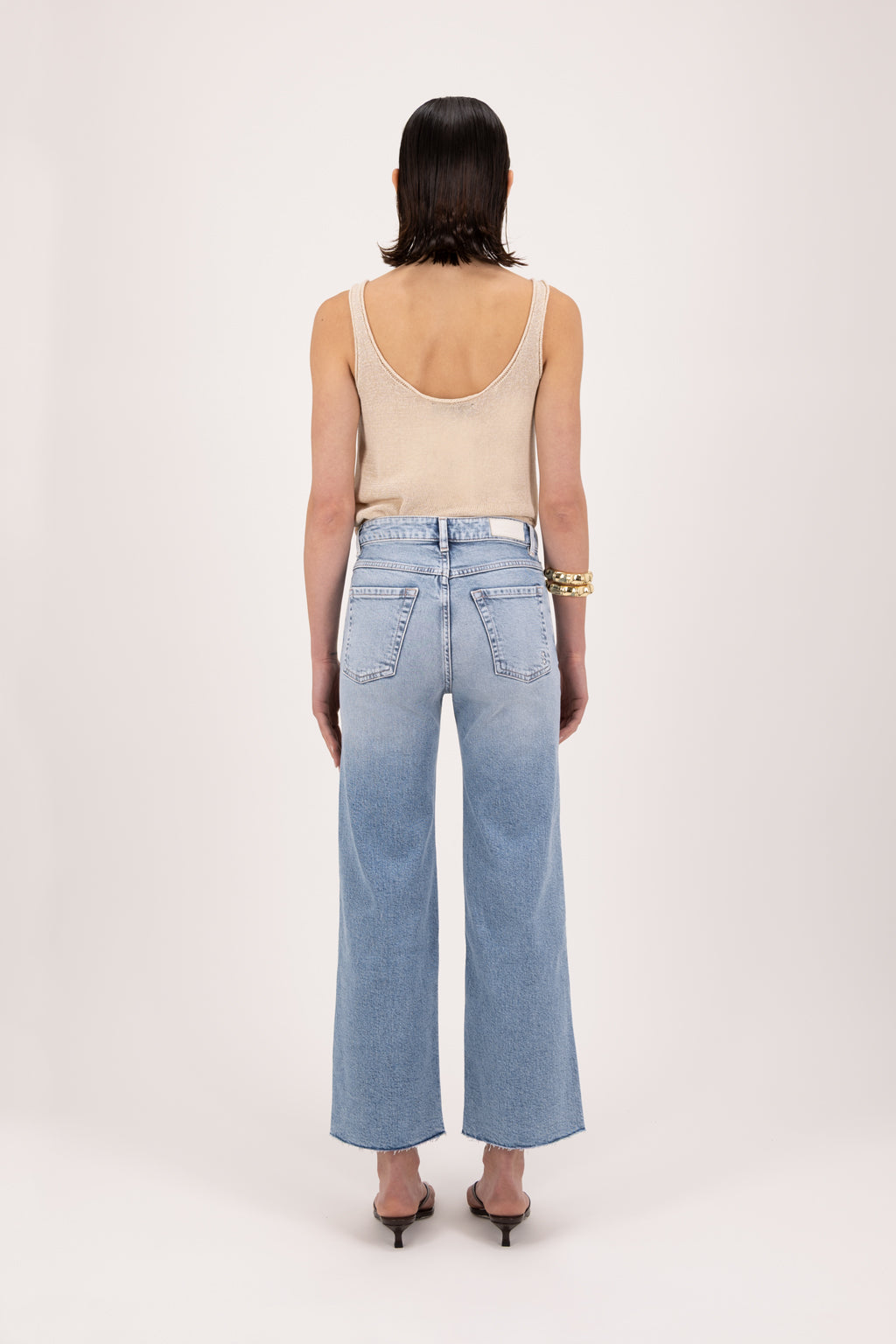 Back view of Angie women’s flared crop jeans in river wash, 99% cotton denim and 1% Elastan fibers, worn by a model with a desert tank top.