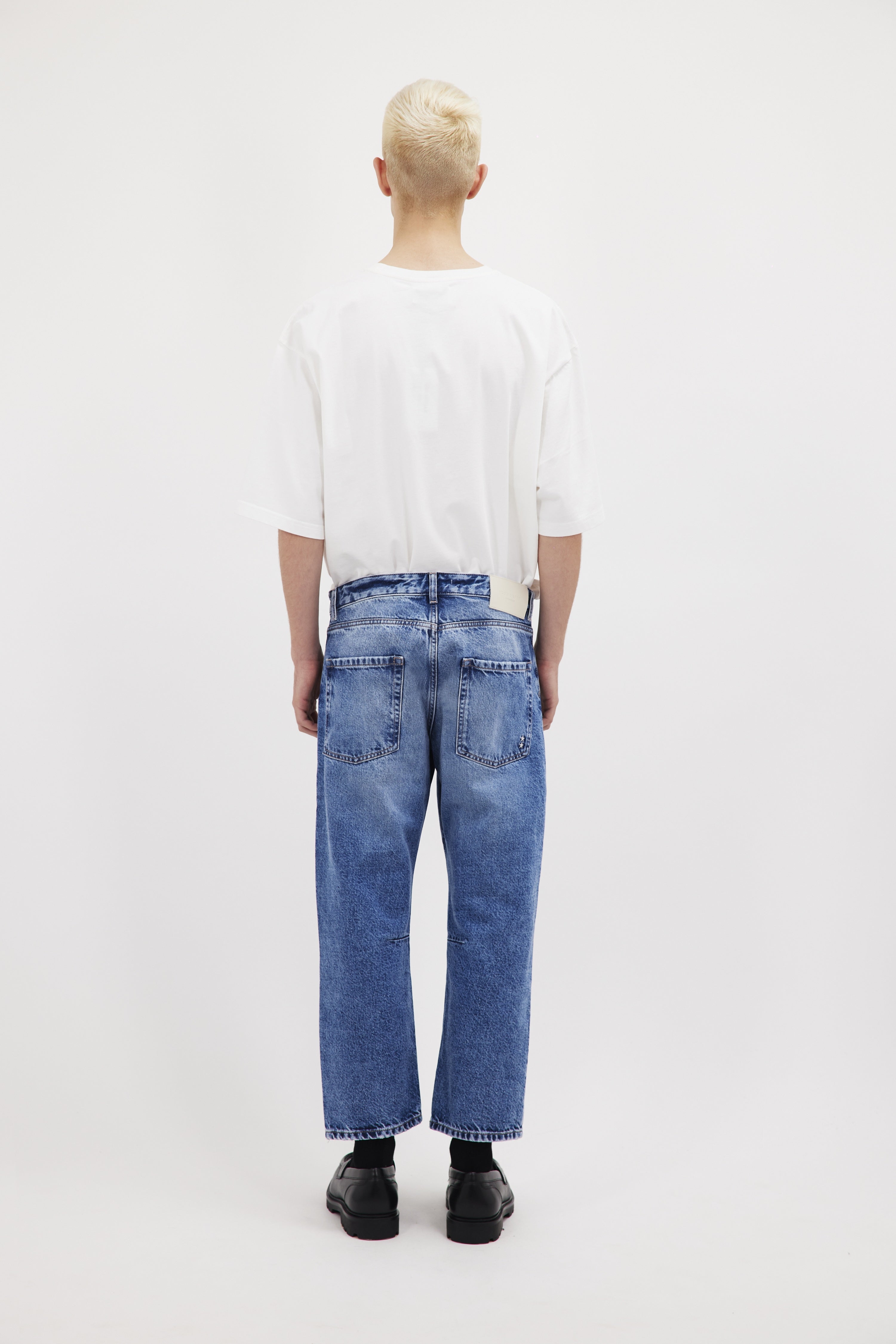 Back view of Ash men's baggy-cut jeans in misty blue wash, 100% rigid cotton denim, worn by a model with a white t-shirt.