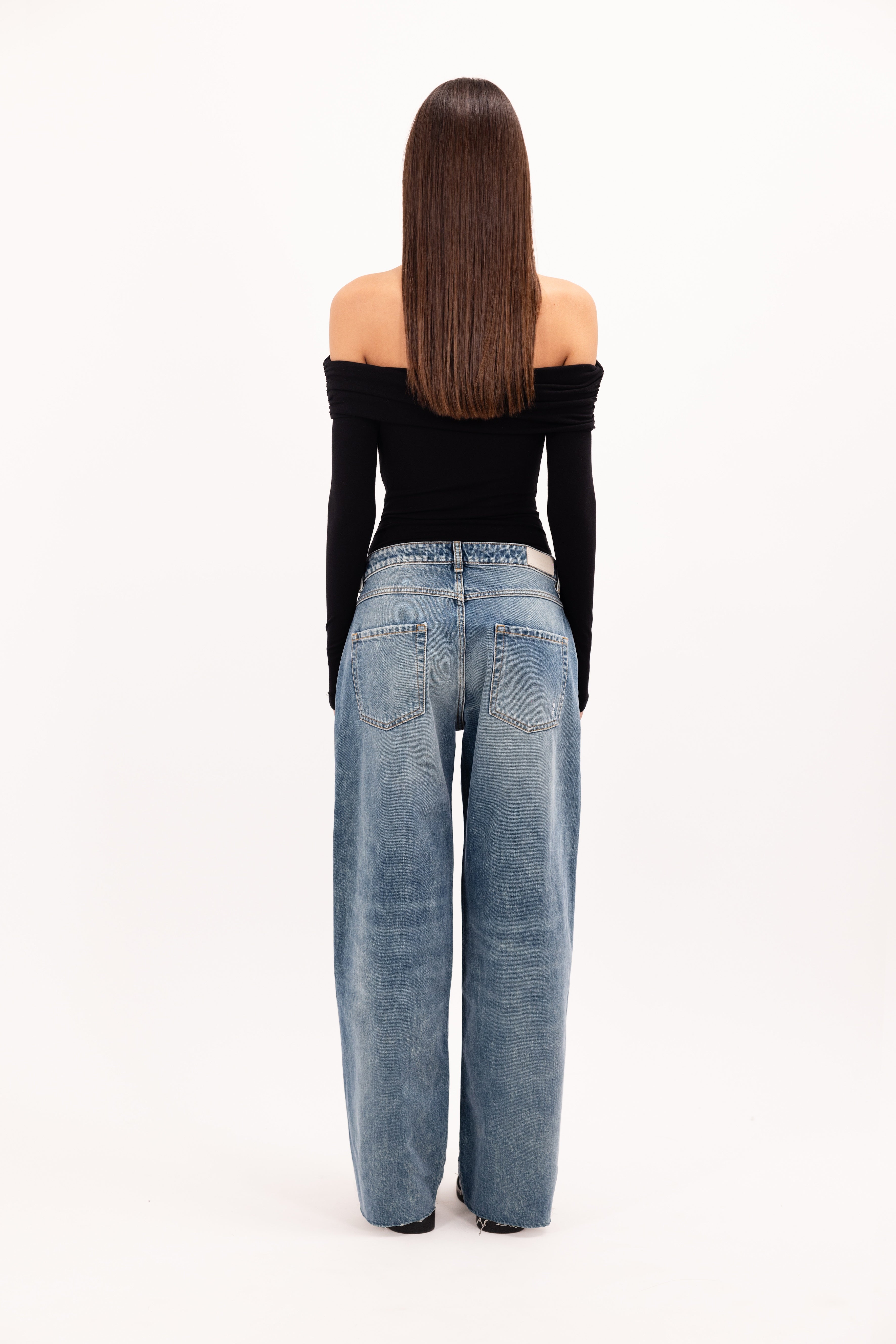 Back view of Bea women’s wide leg jeans in aged stone wash, 100% rigid cotton denim, worn by a model with a black top.