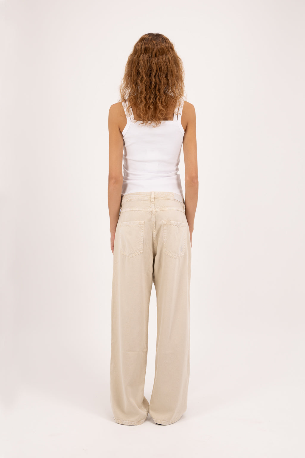 Back view of Bea women’s wide leg jeans in desert wash, 100% rigid soft cotton denim, worn by a model with a white tank top.