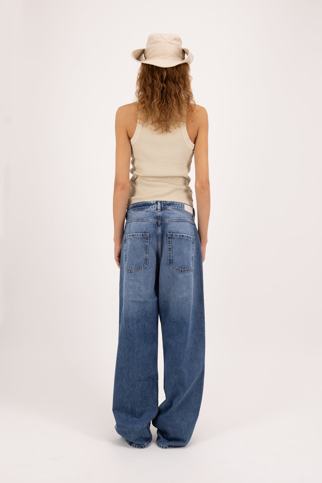 Back view of Bea women’s wide leg jeans in eclipse wash, 100% rigid cotton denim, worn by a model with a beige tank top.