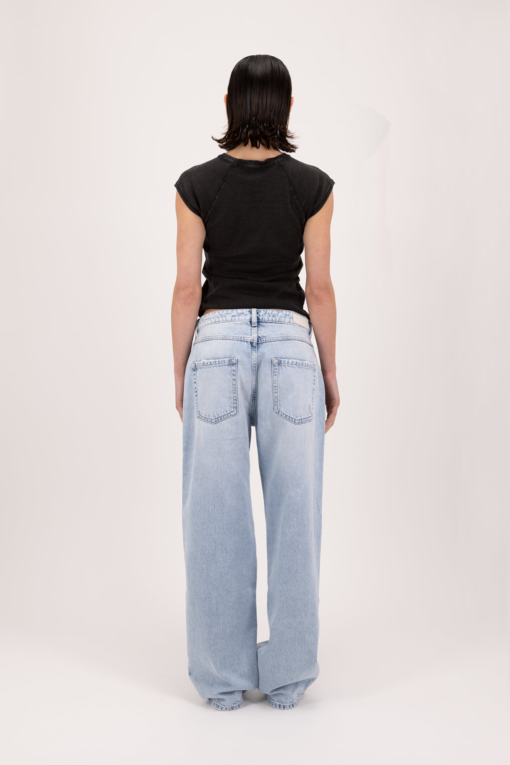 Back view of Bea women’s wide leg jeans in sky blue wash, 100% rigid cotton denim, worn by a model with a black t-shirt.