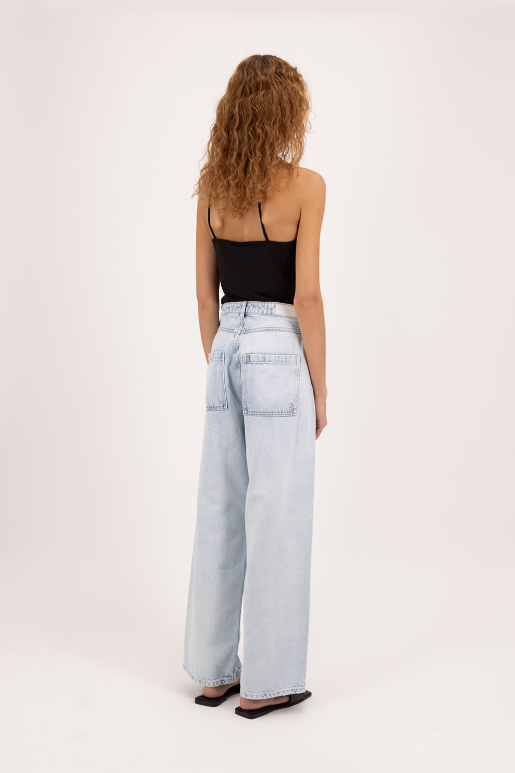 Back view of Bess women’s wide leg jeans in bleached wash, 100% rigid cotton denim, worn by a model with a black top.