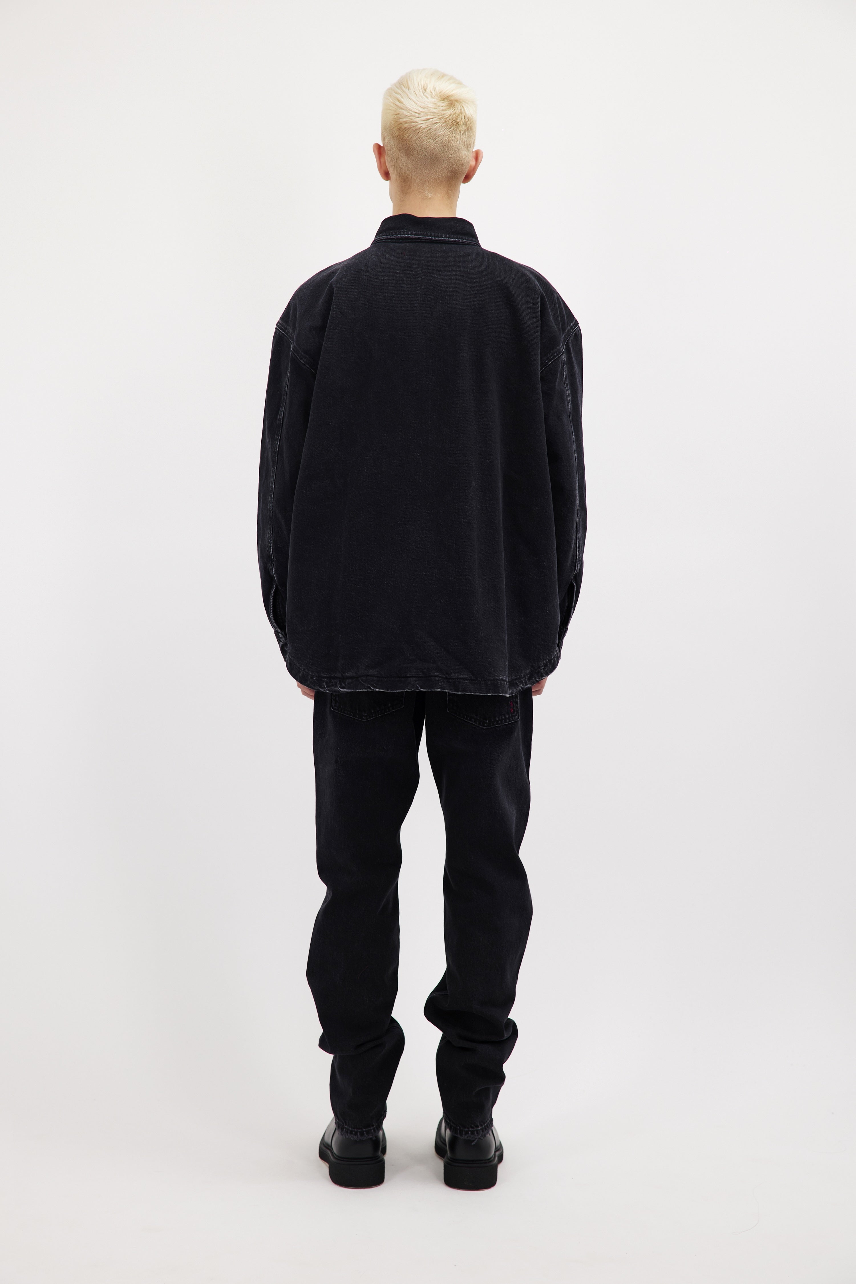 Back view of Billy men’s oversize shirt in graphite black wash, 100% rigid cotton denim, worn by a model with jeans.