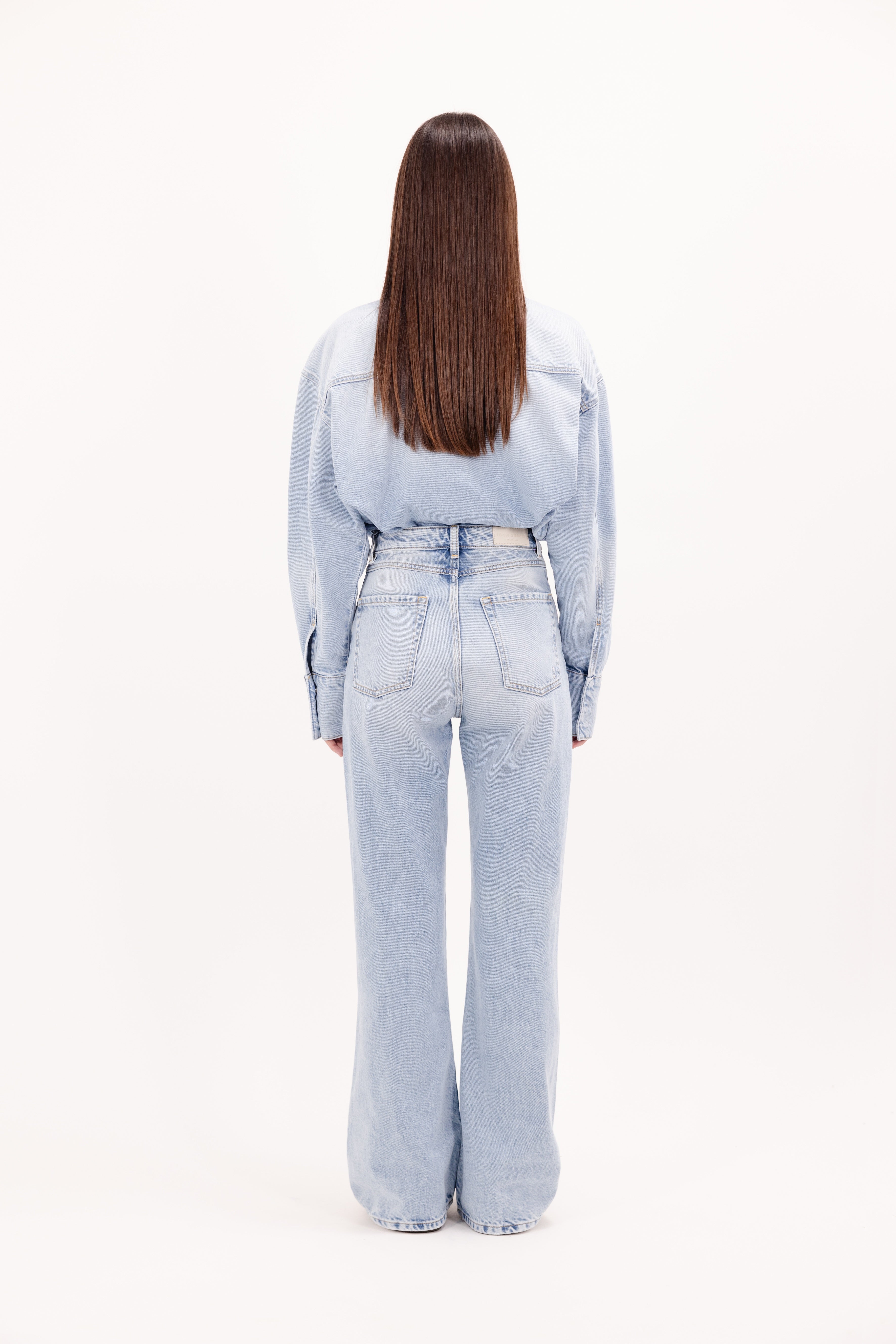 Back view of Blue women’s flared leg jeans in bleached wash, 100% rigid cotton denim, worn by a model with a denim shirt.