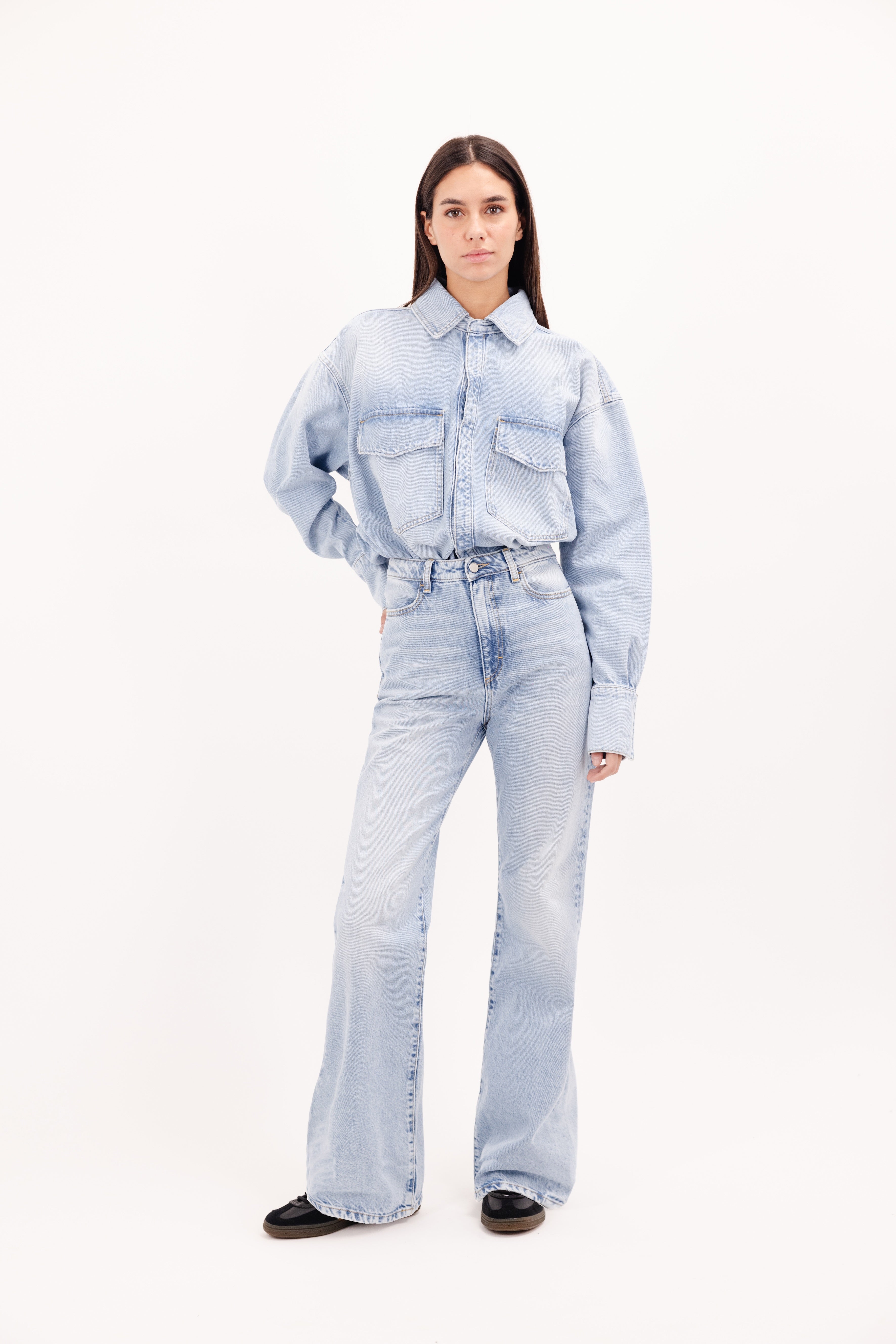 Blue women’s flared leg jeans in bleached wash, 100% rigid cotton denim, worn by a model with a denim shirt.
