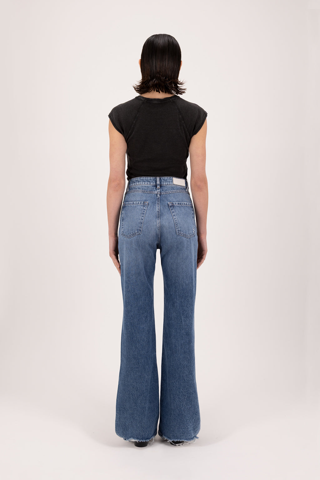 Back view of Blue women’s flared leg jeans in eclipse wash, 100% rigid cotton denim, worn by a model with a black t-shirt.