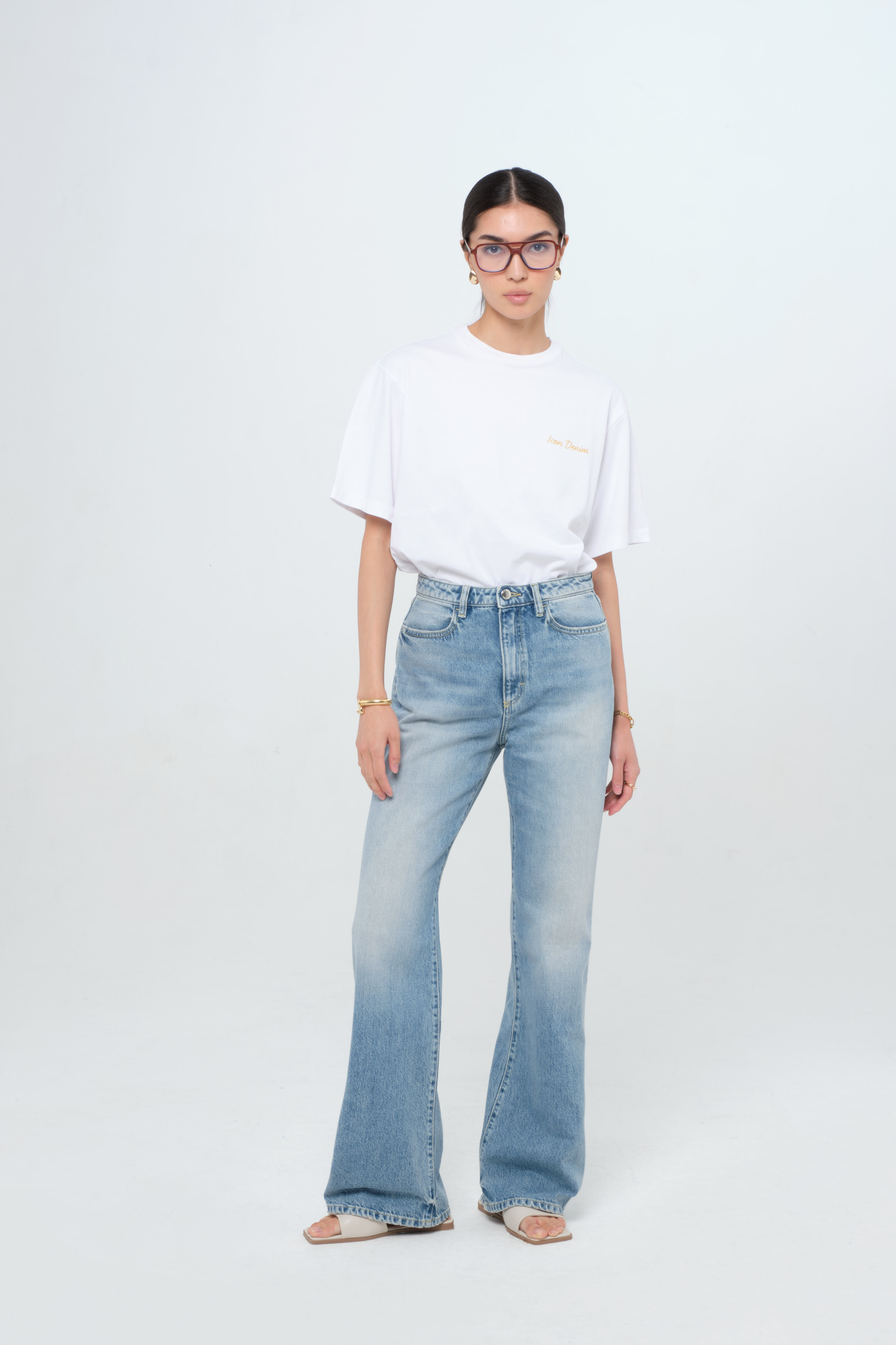 Blue women’s flared leg jeans in smoke blue wash, 100% rigid cotton denim, worn by a model with a white t-shirt.
