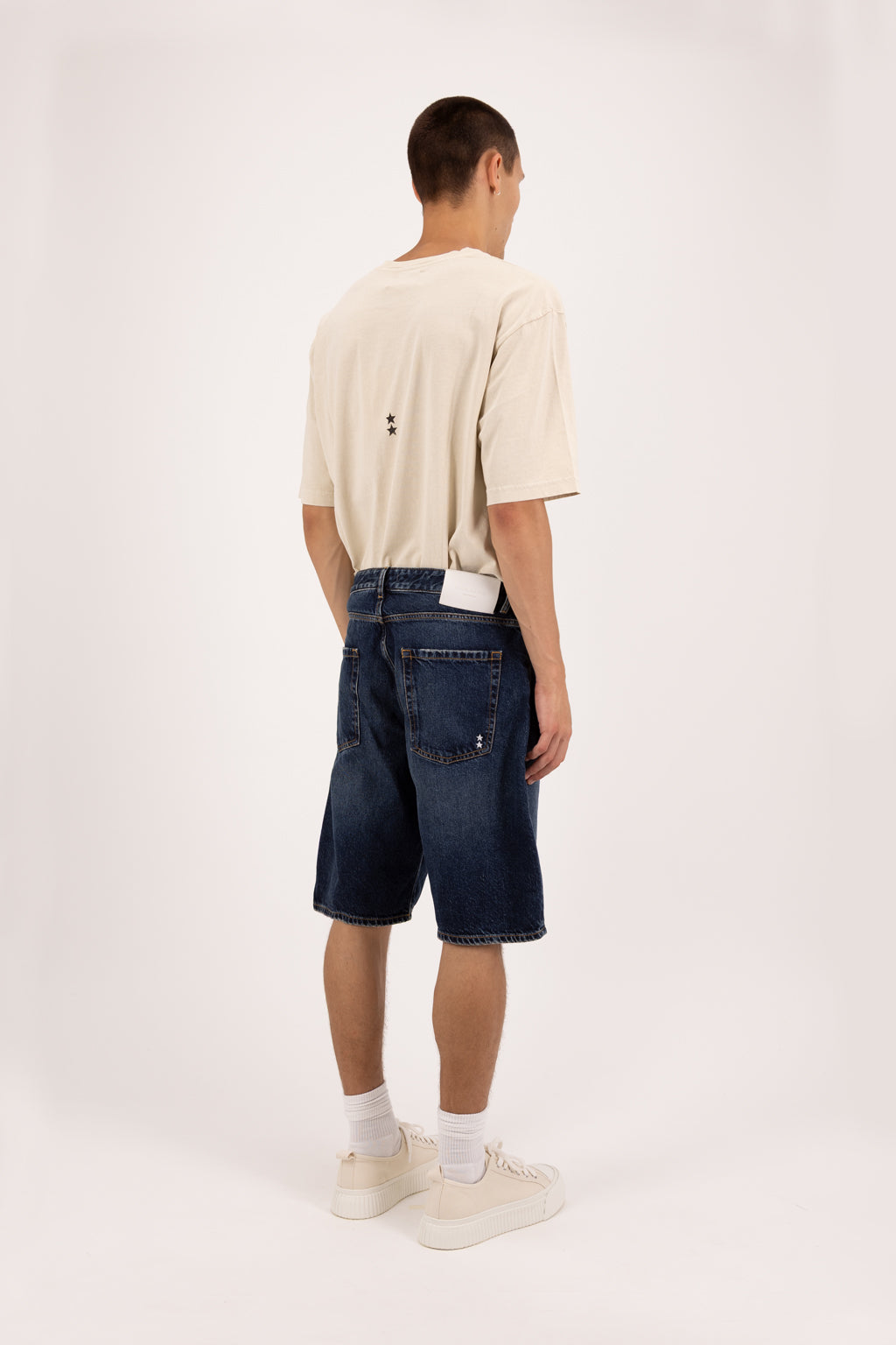 Back view of Bobby men’s short jeans in deep blue wash, 100% rigid cotton denim, worn by a model with a desert t-shirt.