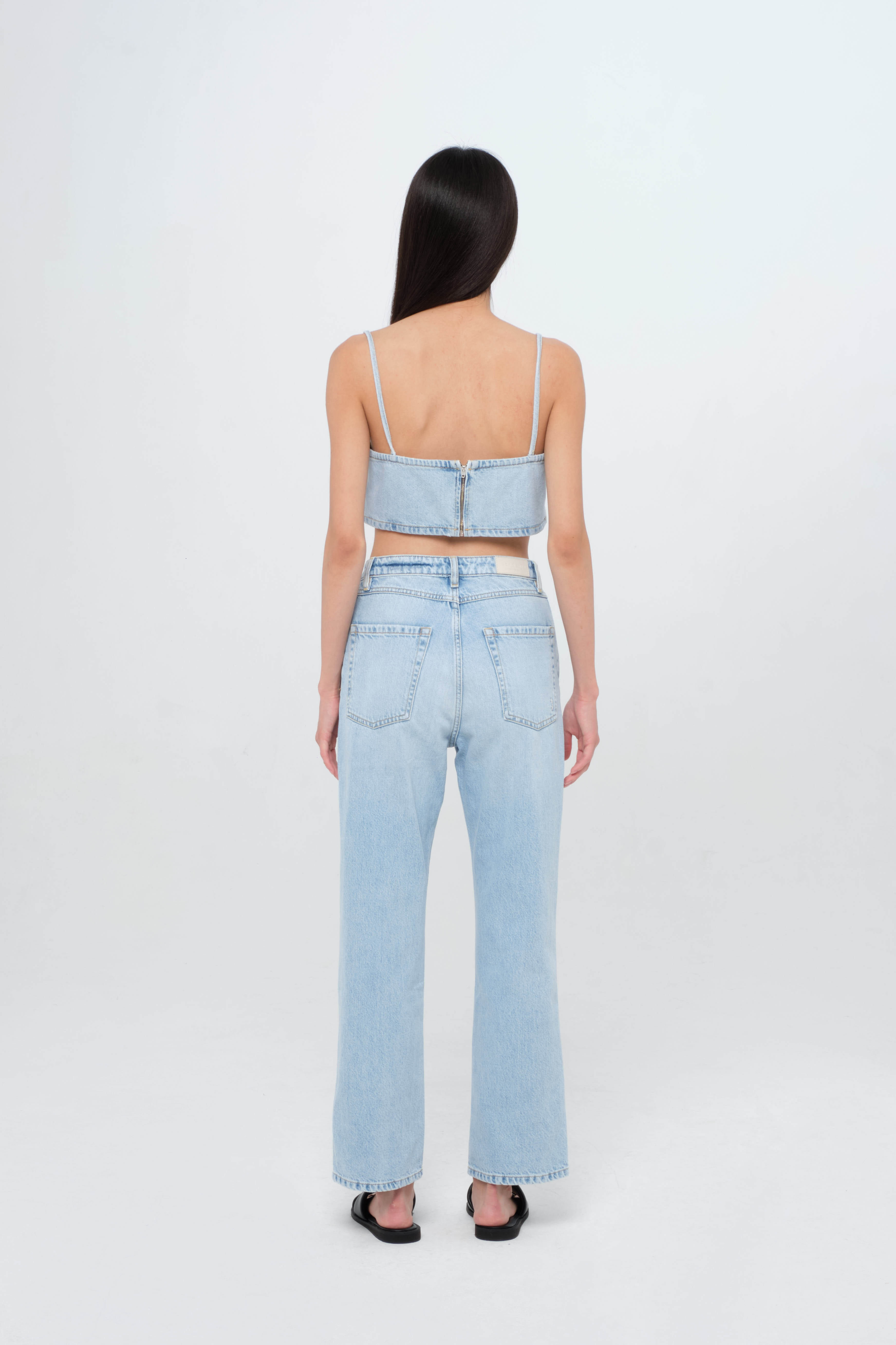 Back view of Cady women’s denim crop top in light wash, 100% rigid cotton denim, worn by a model with jeans.
