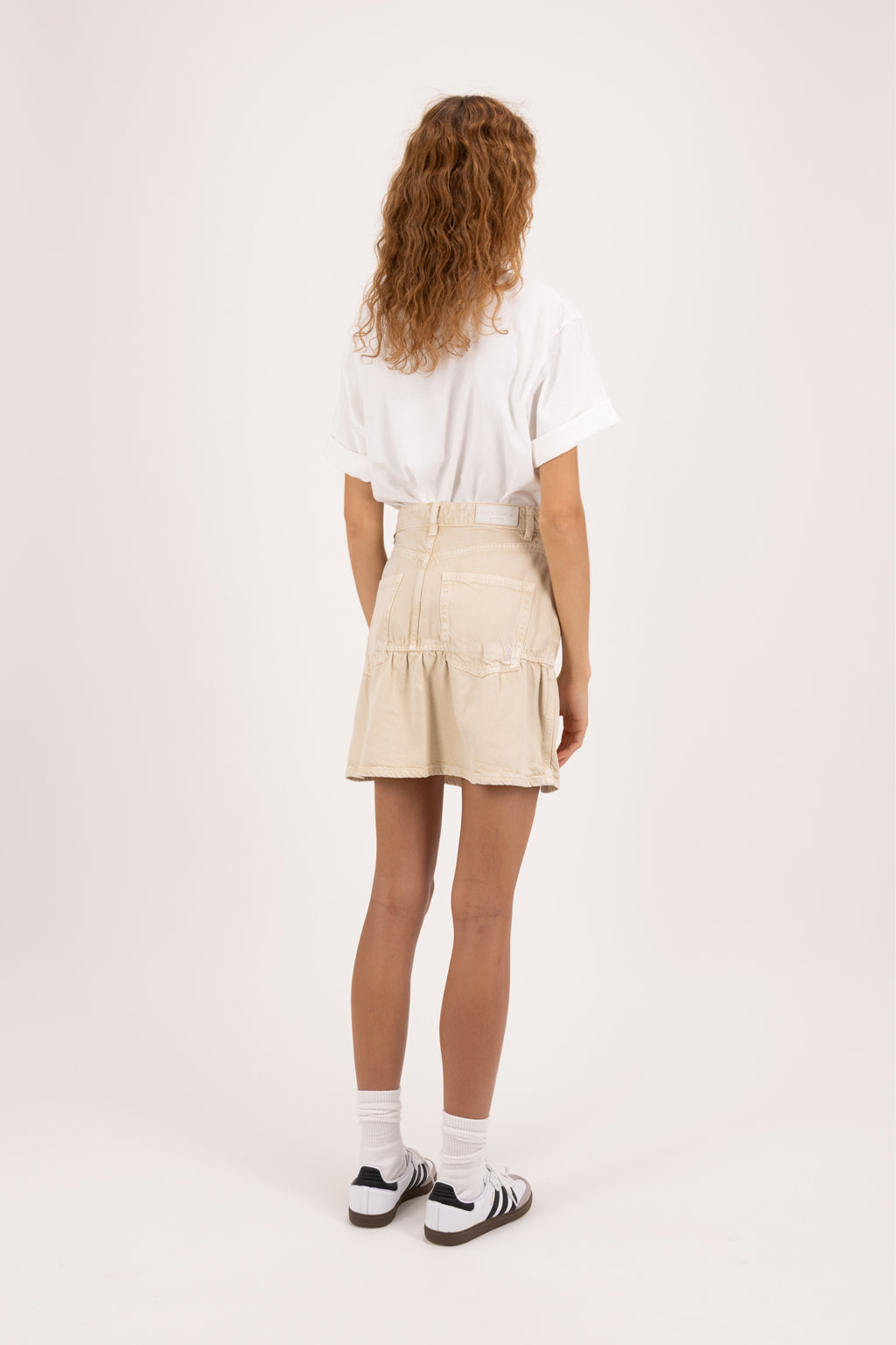 Back view of Caly women’s regular skirt jeans in desert wash, 100% rigid soft cotton denim, worn by a model with a white t-shirt.