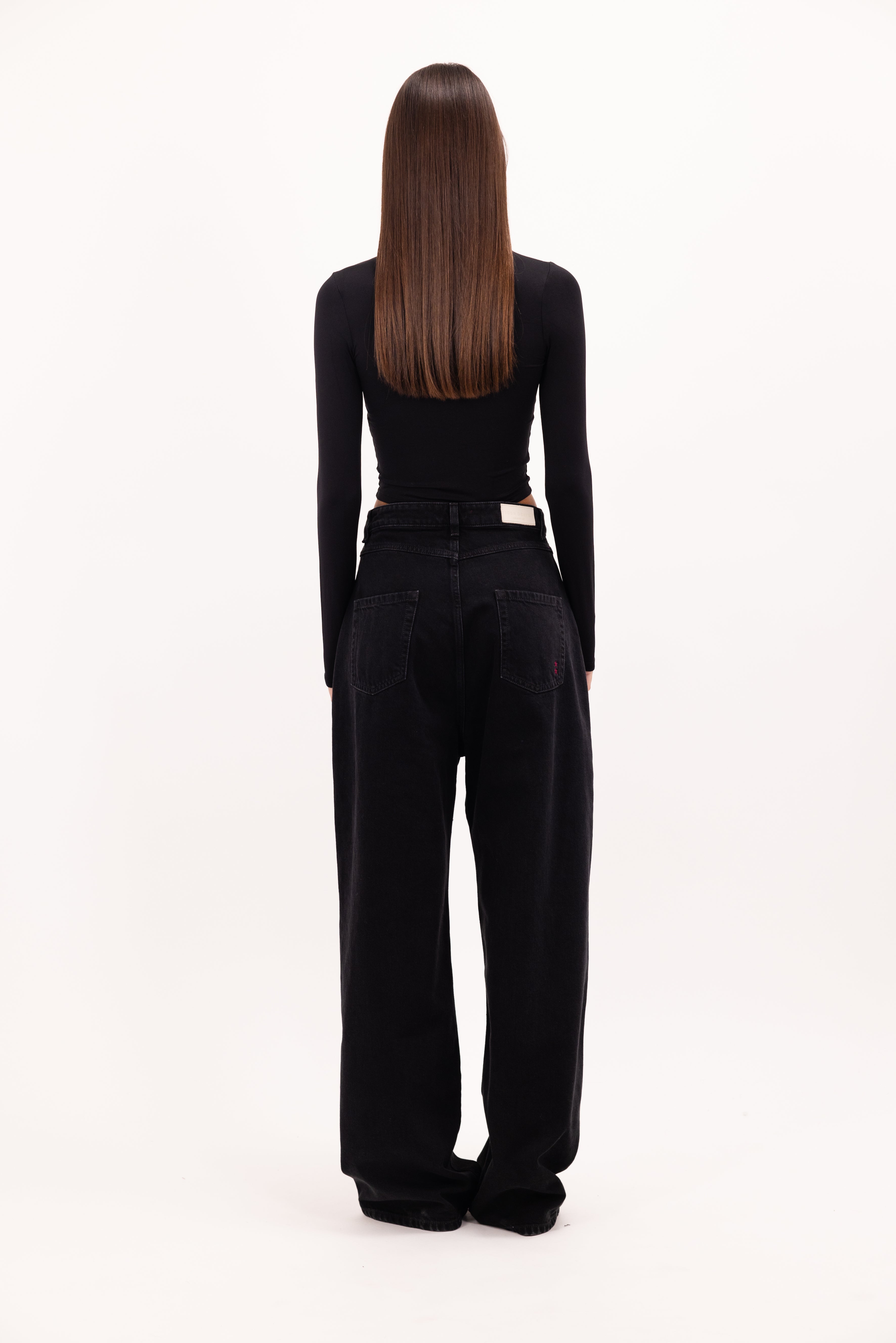 Back view of Coco women’s wide leg jeans in graphite black wash, 100% rigid cotton denim, worn by a model with a black top.