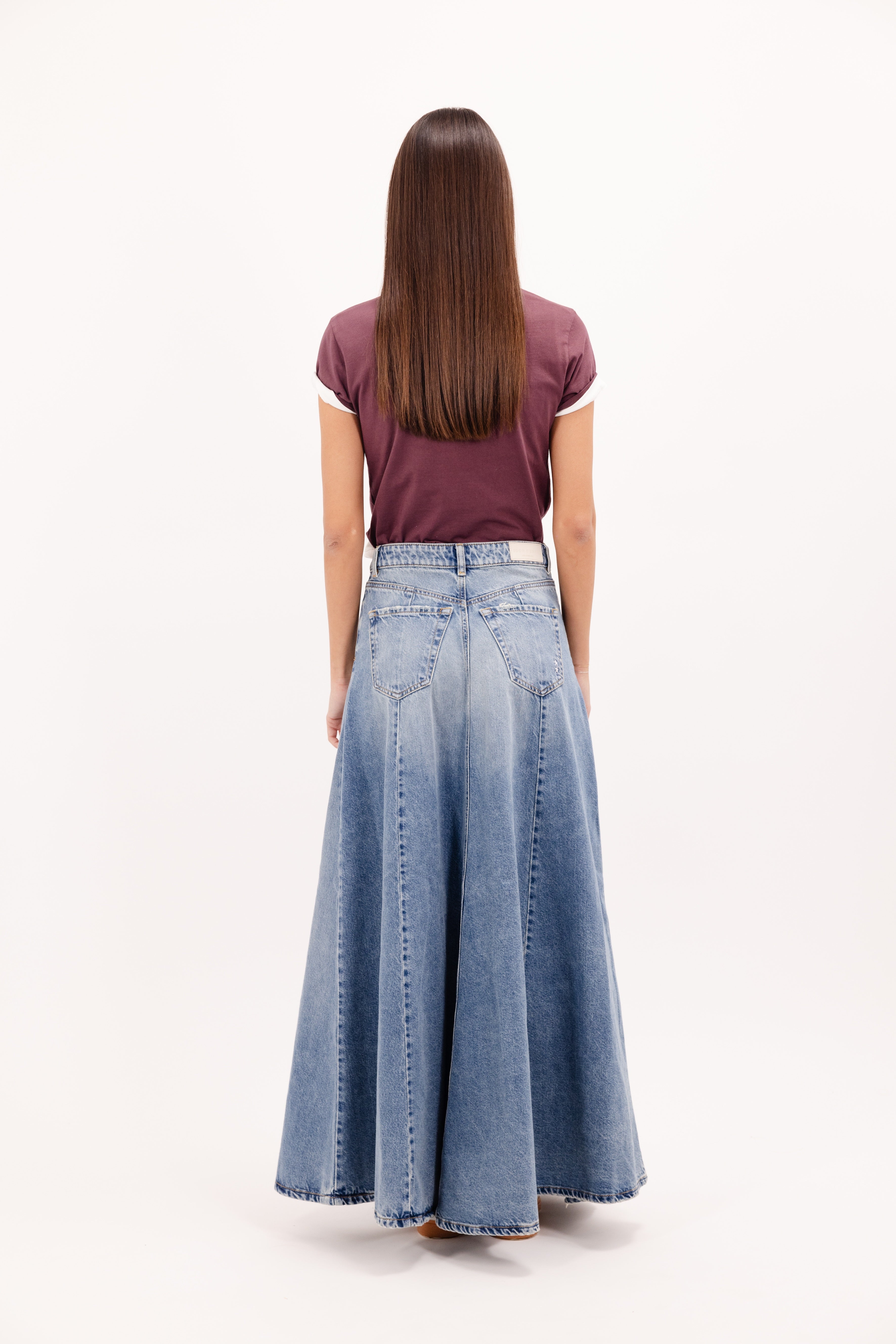Back view of Cora women’s long skirt in smoke blue wash, 100% rigid cotton denim, worn by a model with a cherry t-shirt.
