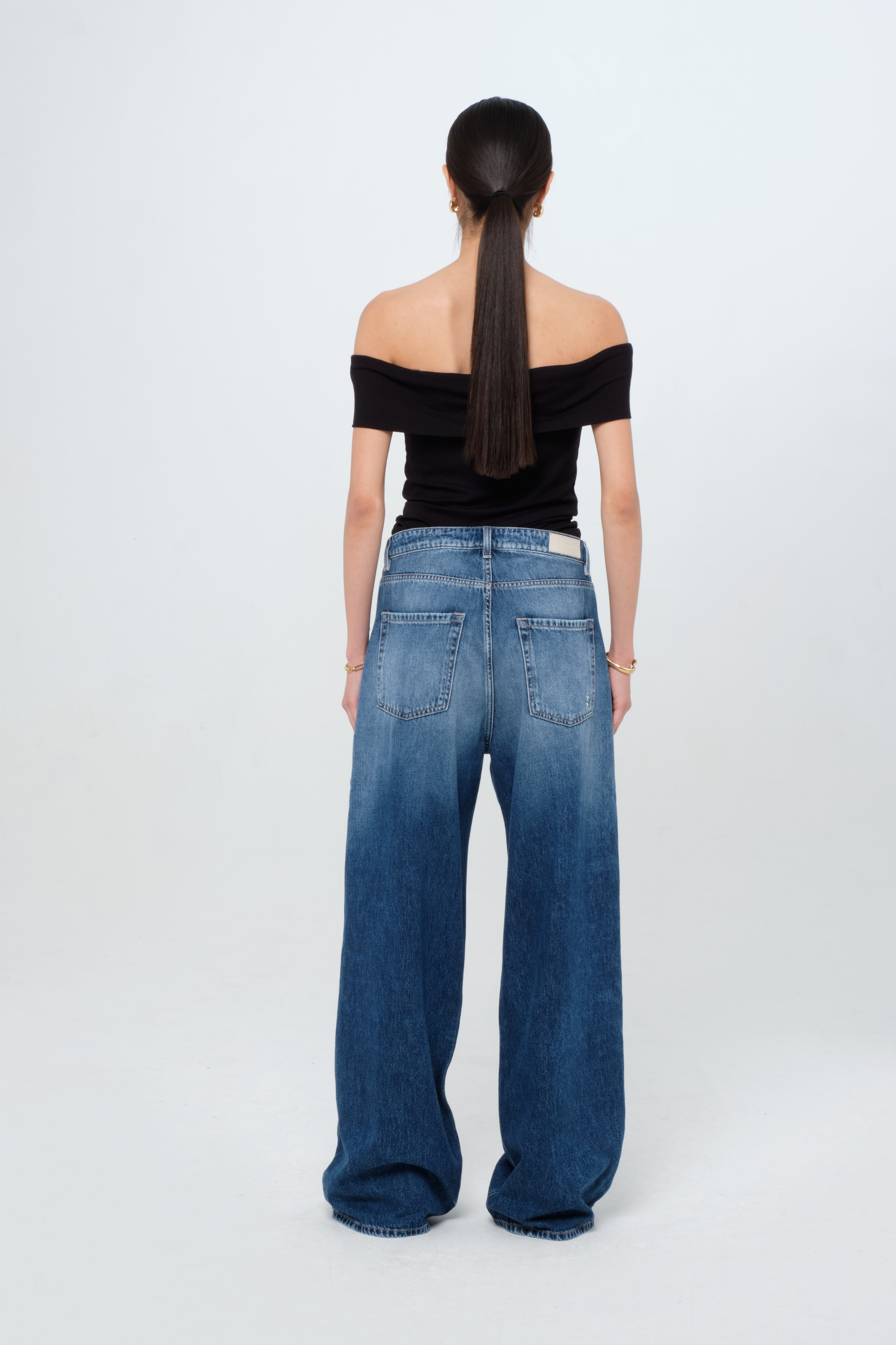 Back view of Debby women’s wide leg jeans in dark wash, 100% rigid cotton denim, worn by a model with a black top.