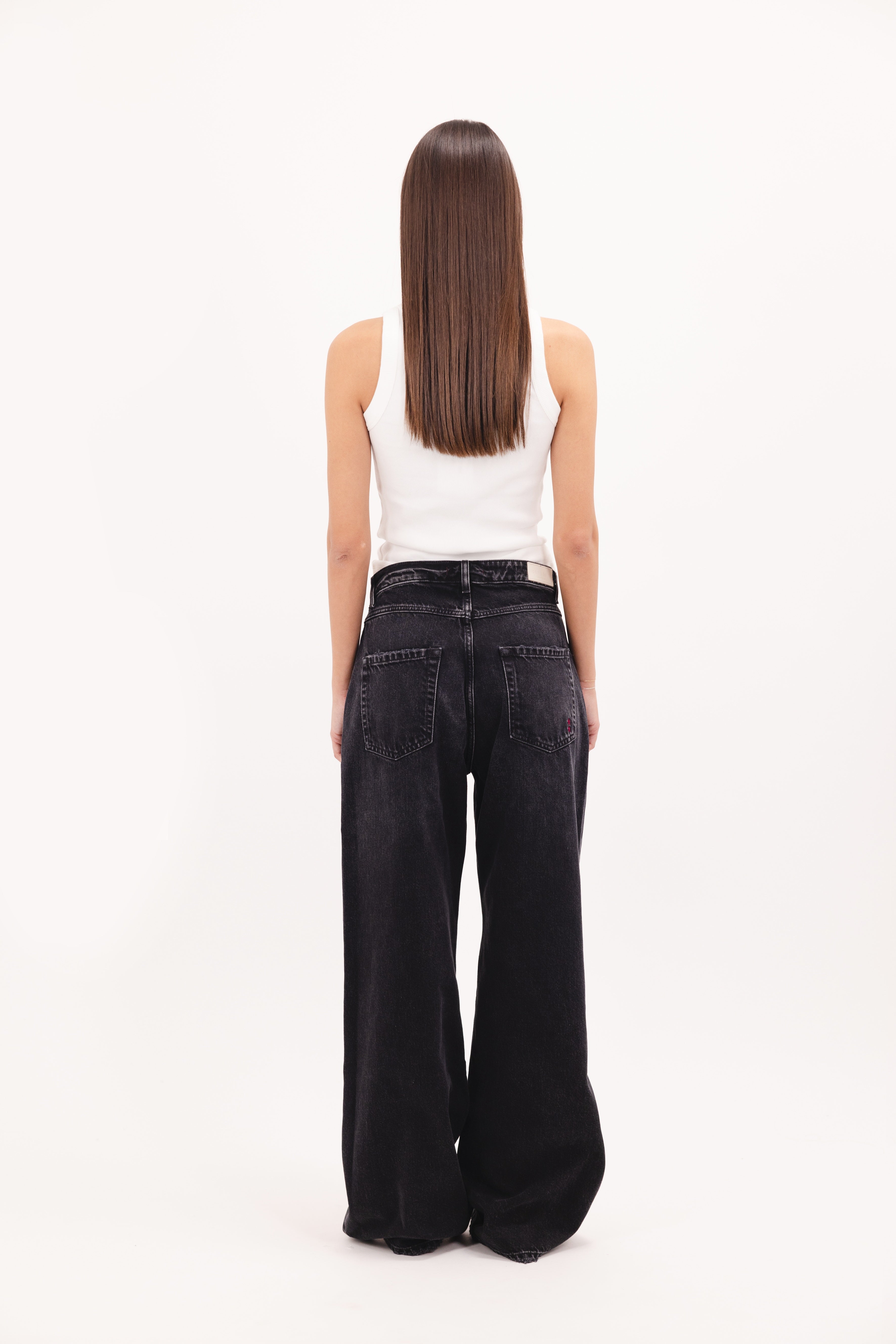 Back view of Debby women’s wide leg jeans in graphite black wash, 100% rigid cotton denim, worn by a model with a white top.