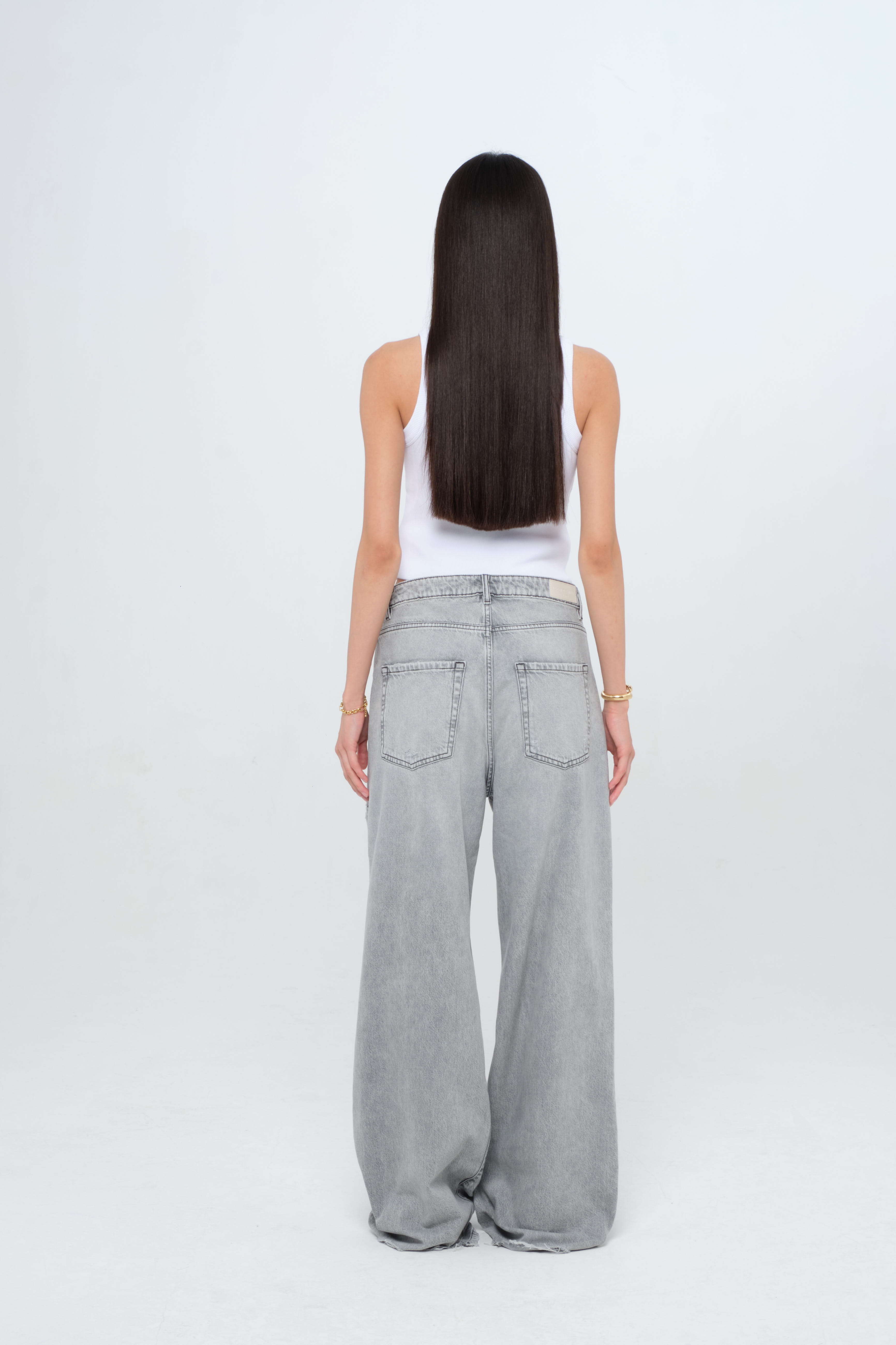Back view of Debby women’s wide leg jeans in gray wash, 100% rigid cotton denim, worn by a model with a white tank top.