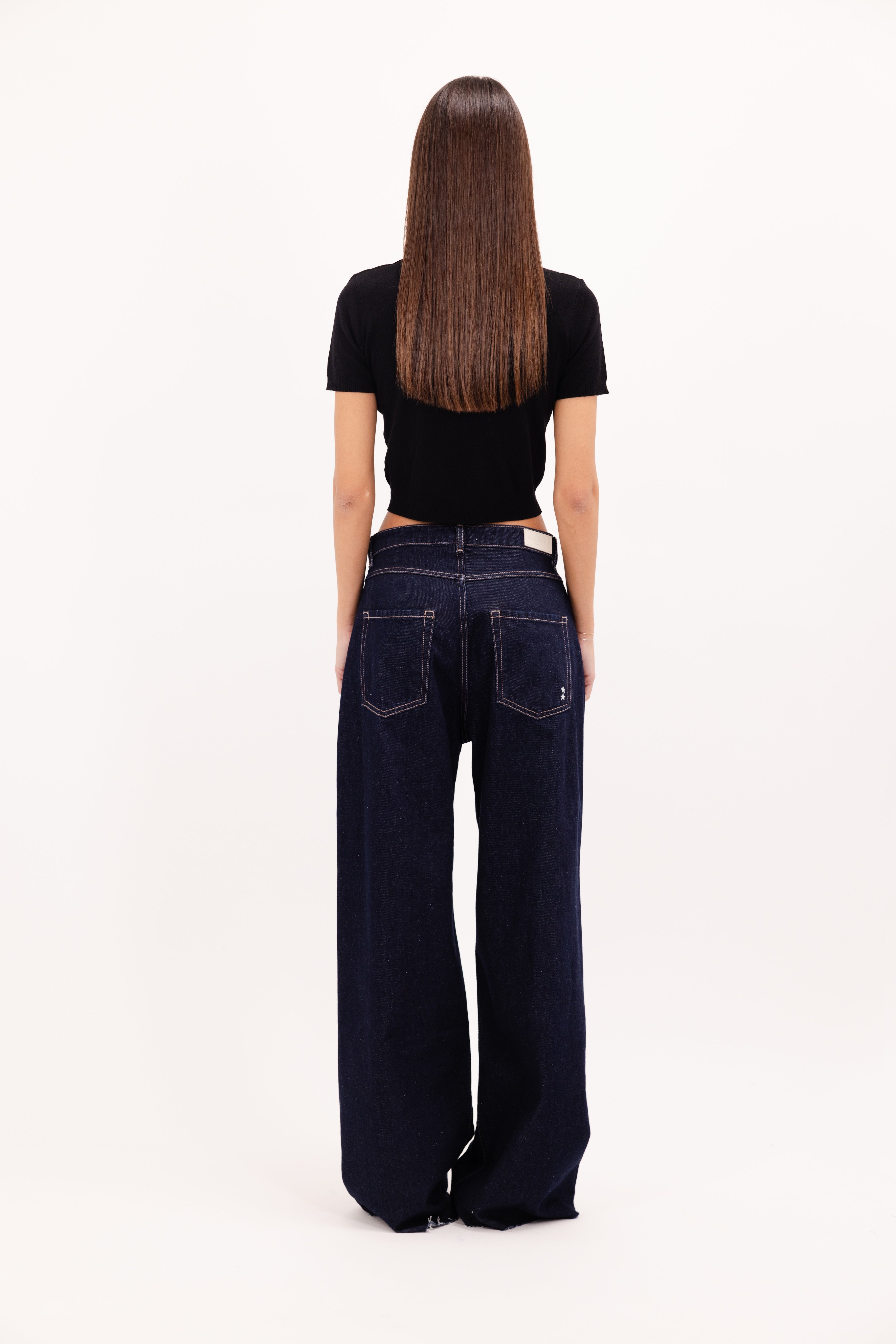 Back view of Debby women’s wide leg jeans in indigo raw wash, 100% rigid cotton denim, worn by a model with a black top.
